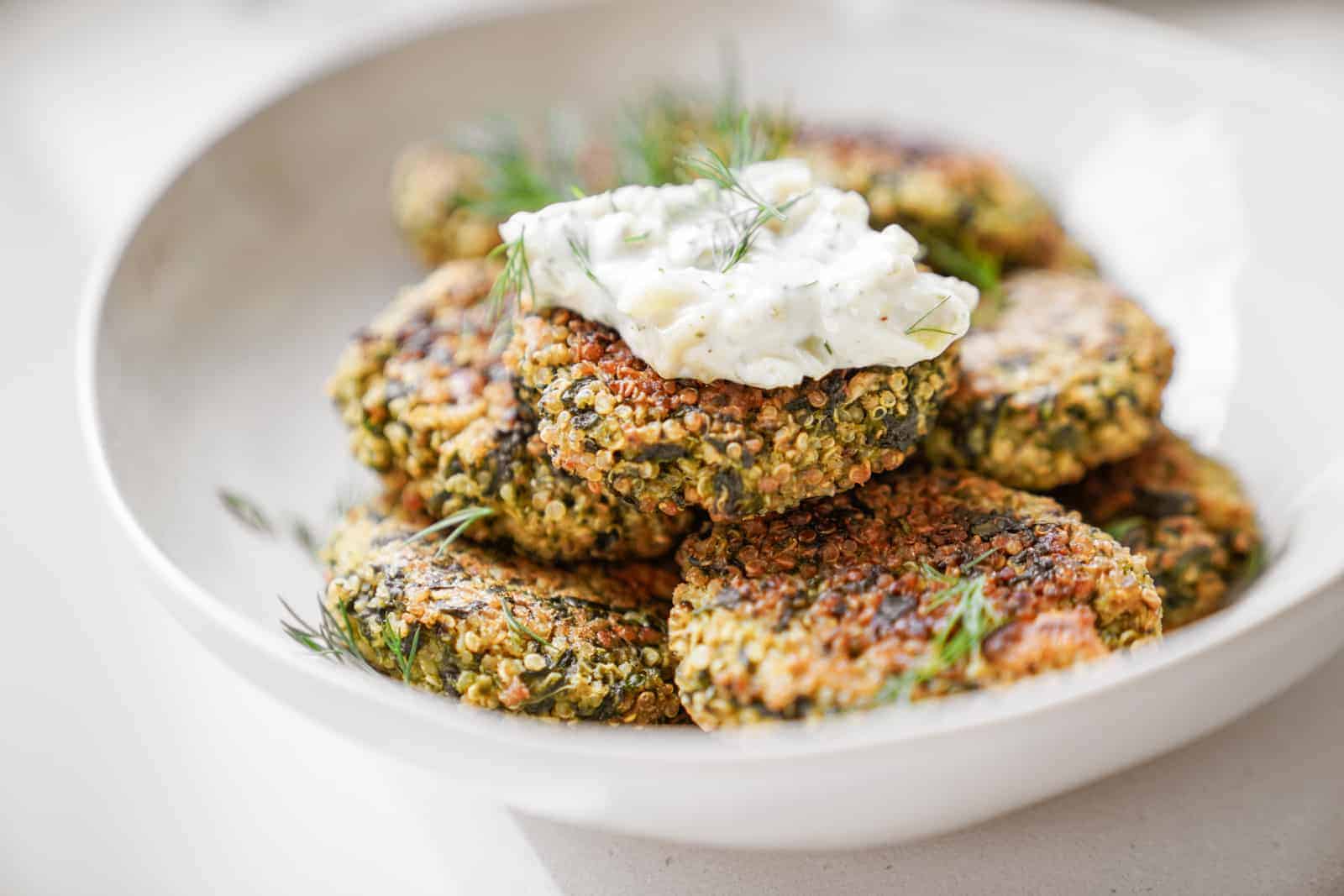 Close up of quinoa and spinach patties in serving dish topped with aioli. 