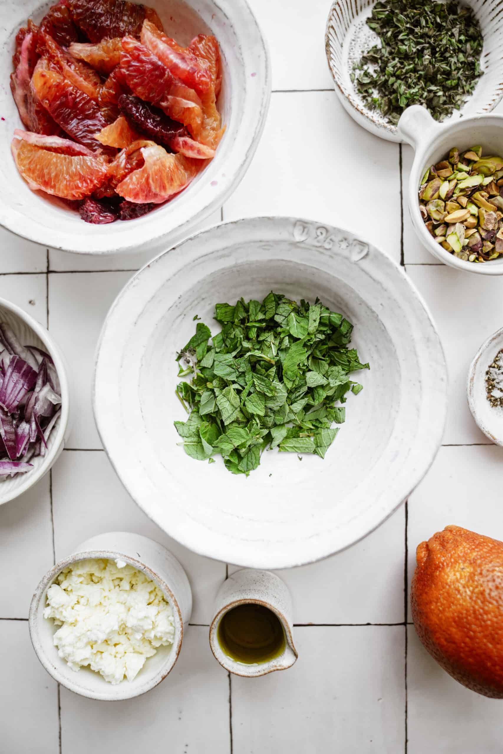 chopped and prepped ingredients in white bowls on white backdrop for blood orange salad 