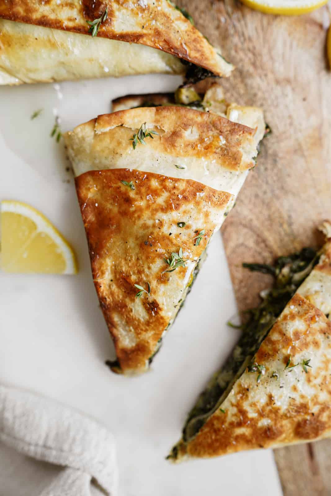 Trendy spinach wrap made greek-style cut into triangles on countertop.