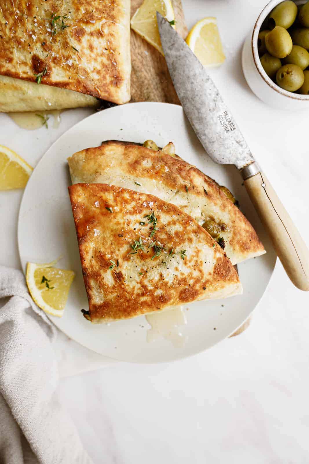 Trendy spinach wrap made greek-style cut into triangles on serving dish next to knife