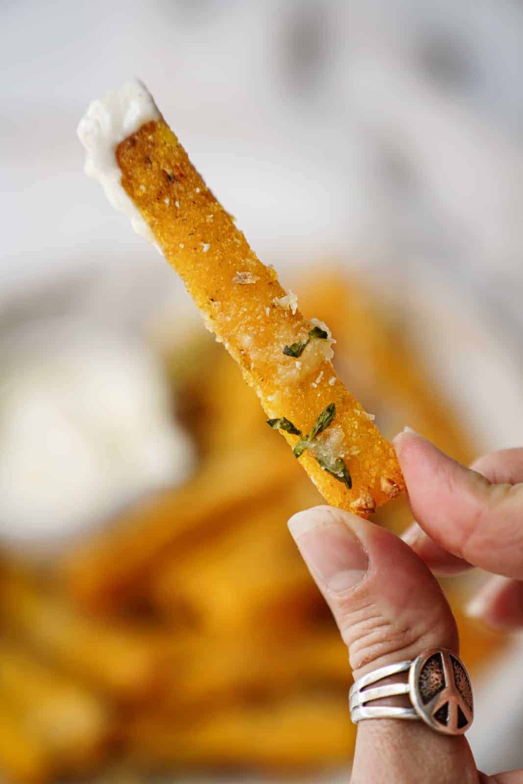 Hand holding a vegan polenta fry dipped in vegan aioli