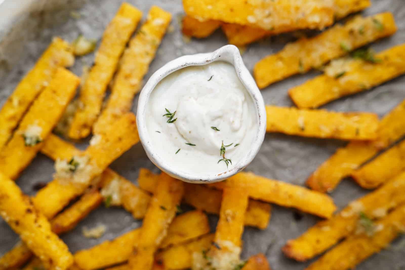 Close-up of vegan polenta fries on a baking sheet with aioli dipping sauce