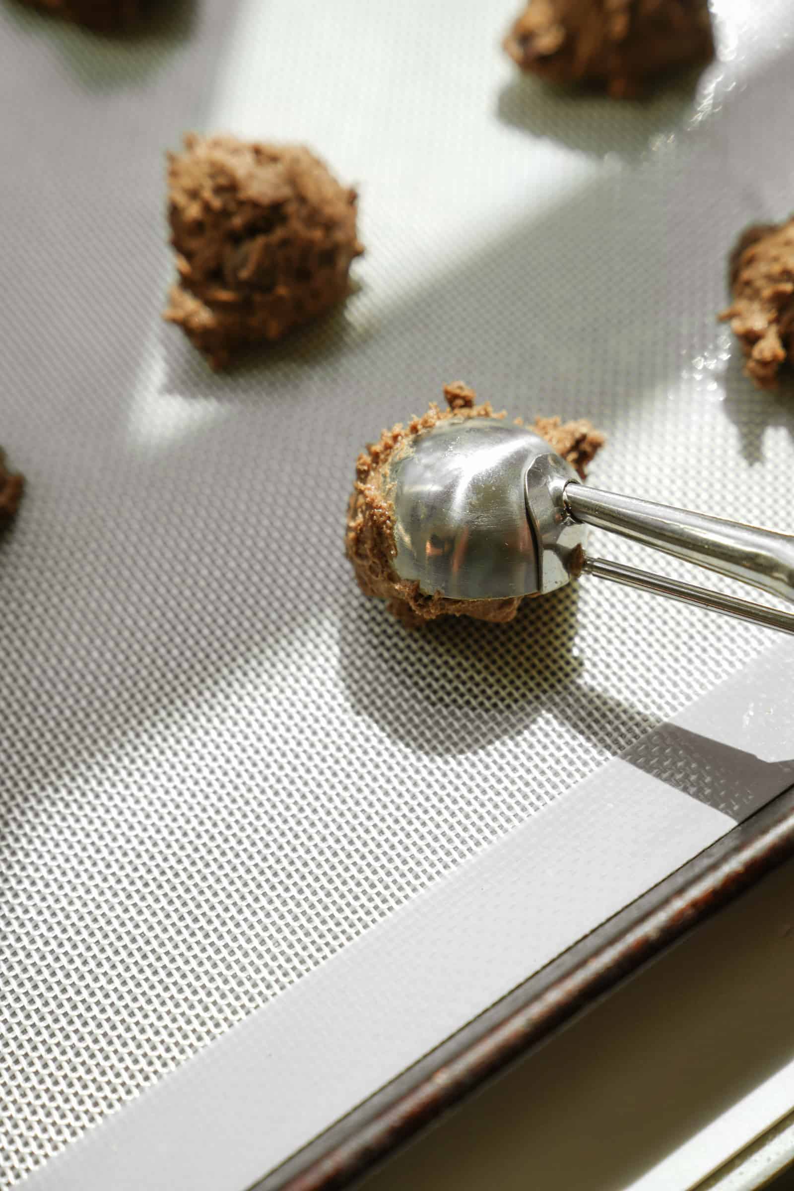 Ice cream scoop scooping dough onto baking sheet for vegan cookies