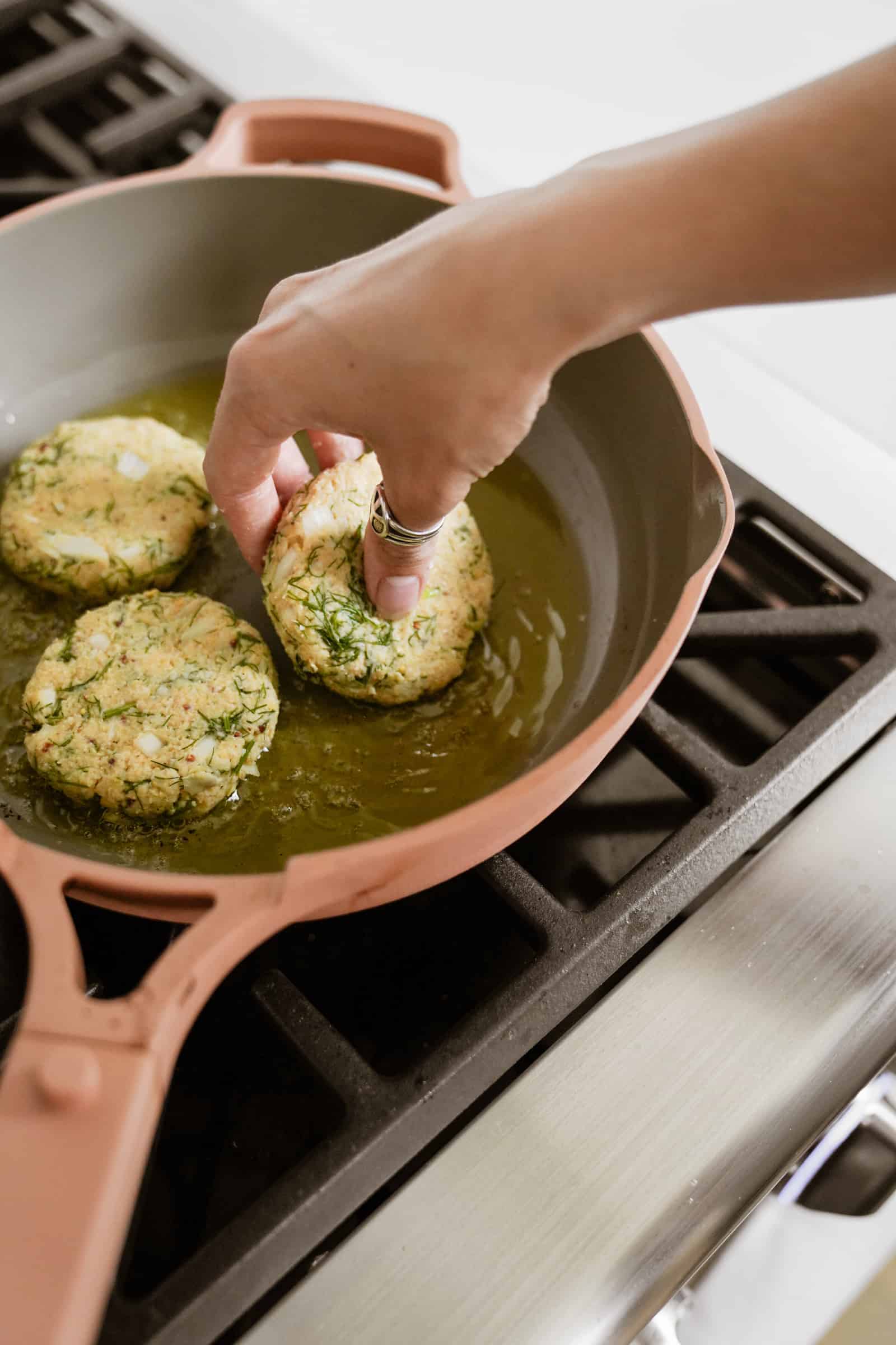 Hand placing crab cake onto a heated pan