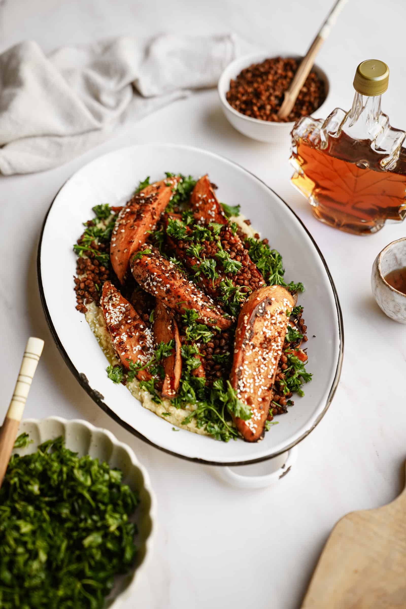 Roasted sweet potatoes on a dish with fresh herbs, surrounded by ingredients