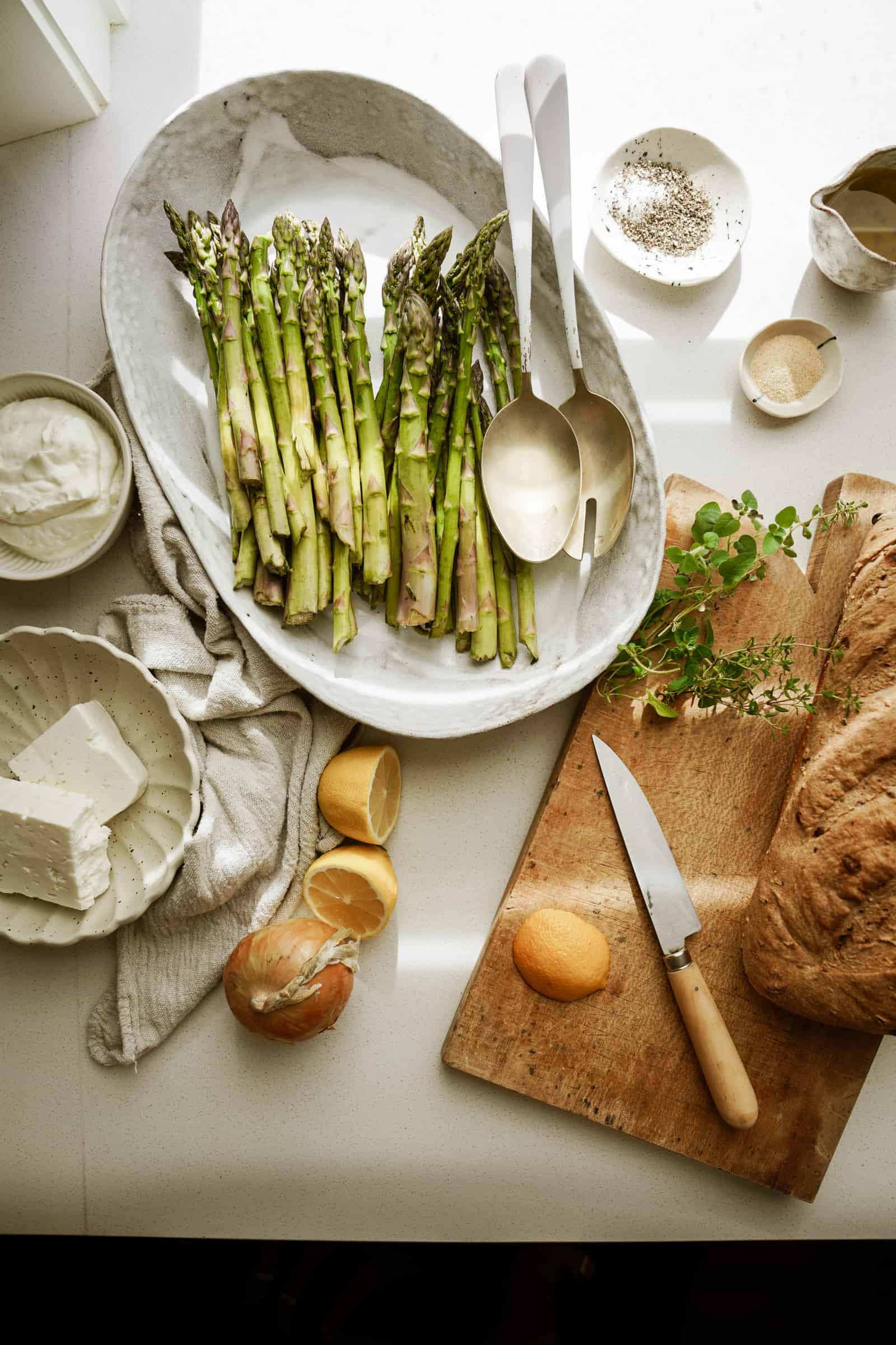 Greek marinated asparagus on a serving dish surrounded by fresh ingredients