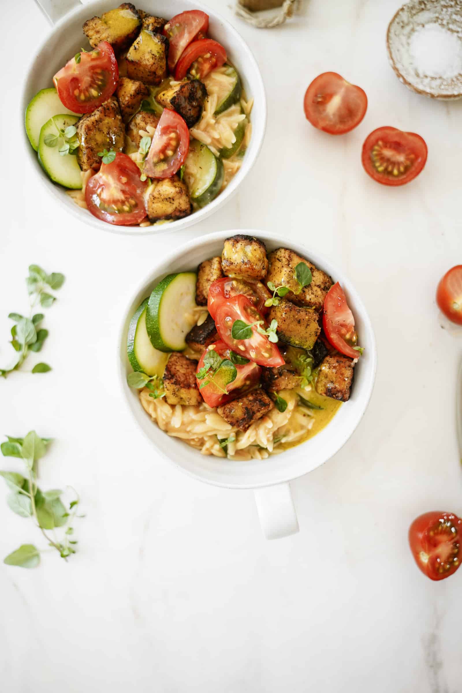 Greek tempeh with creamy orzo in a white bowl on a white counter