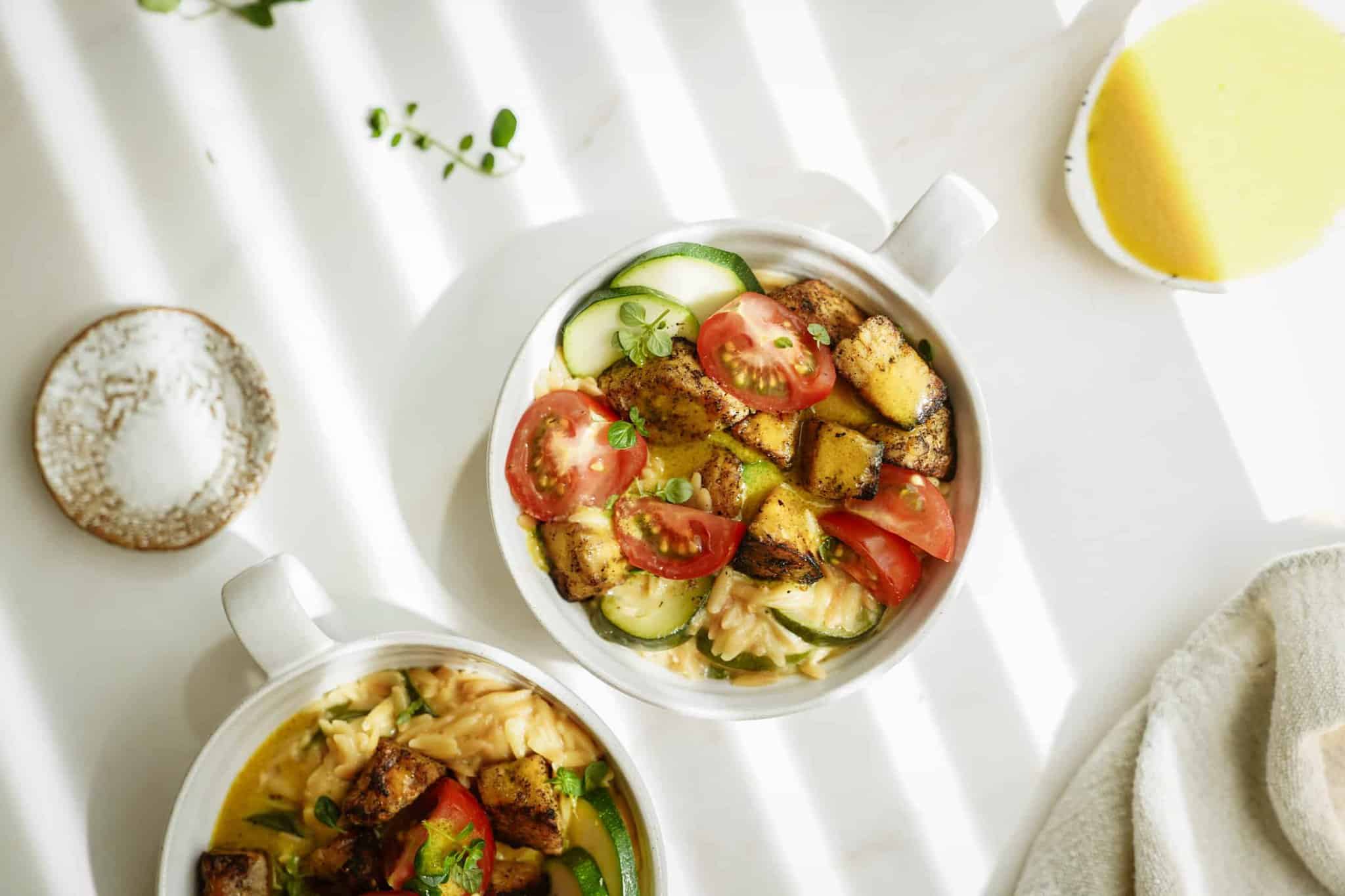 Greek tempeh with creamy orzo in a white bowl on a white counter