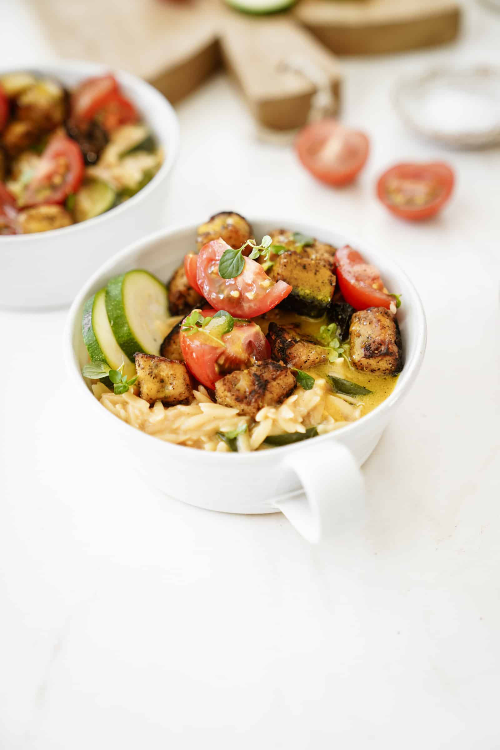Greek tempeh with creamy orzo in a white bowl on a white counter