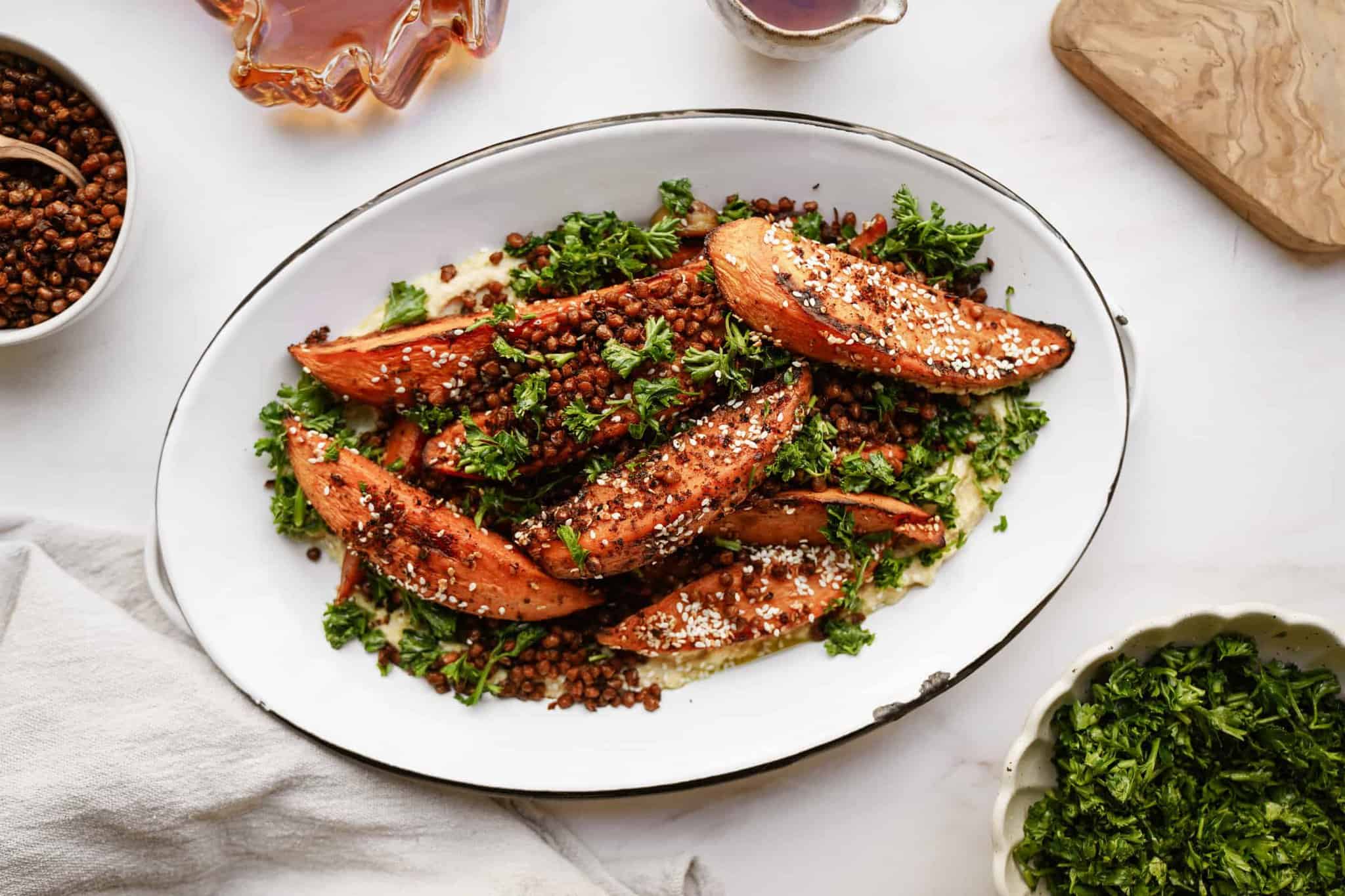 Roasted sweet potatoes on a dish with fresh herbs, surrounded by ingredients