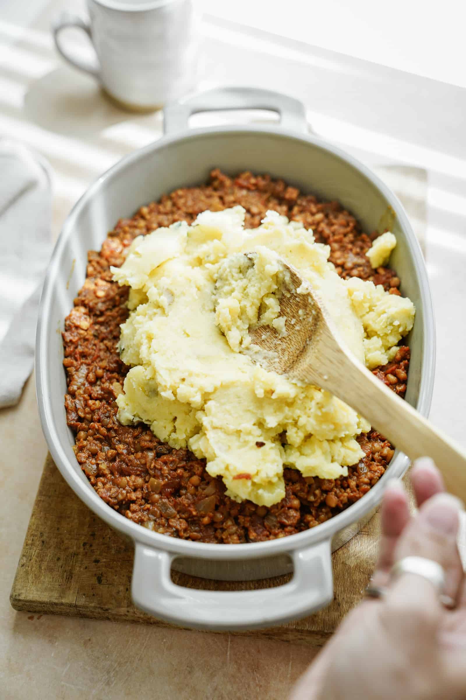 Vegan shepherds pie in a pan with mashed potatoes being put over top