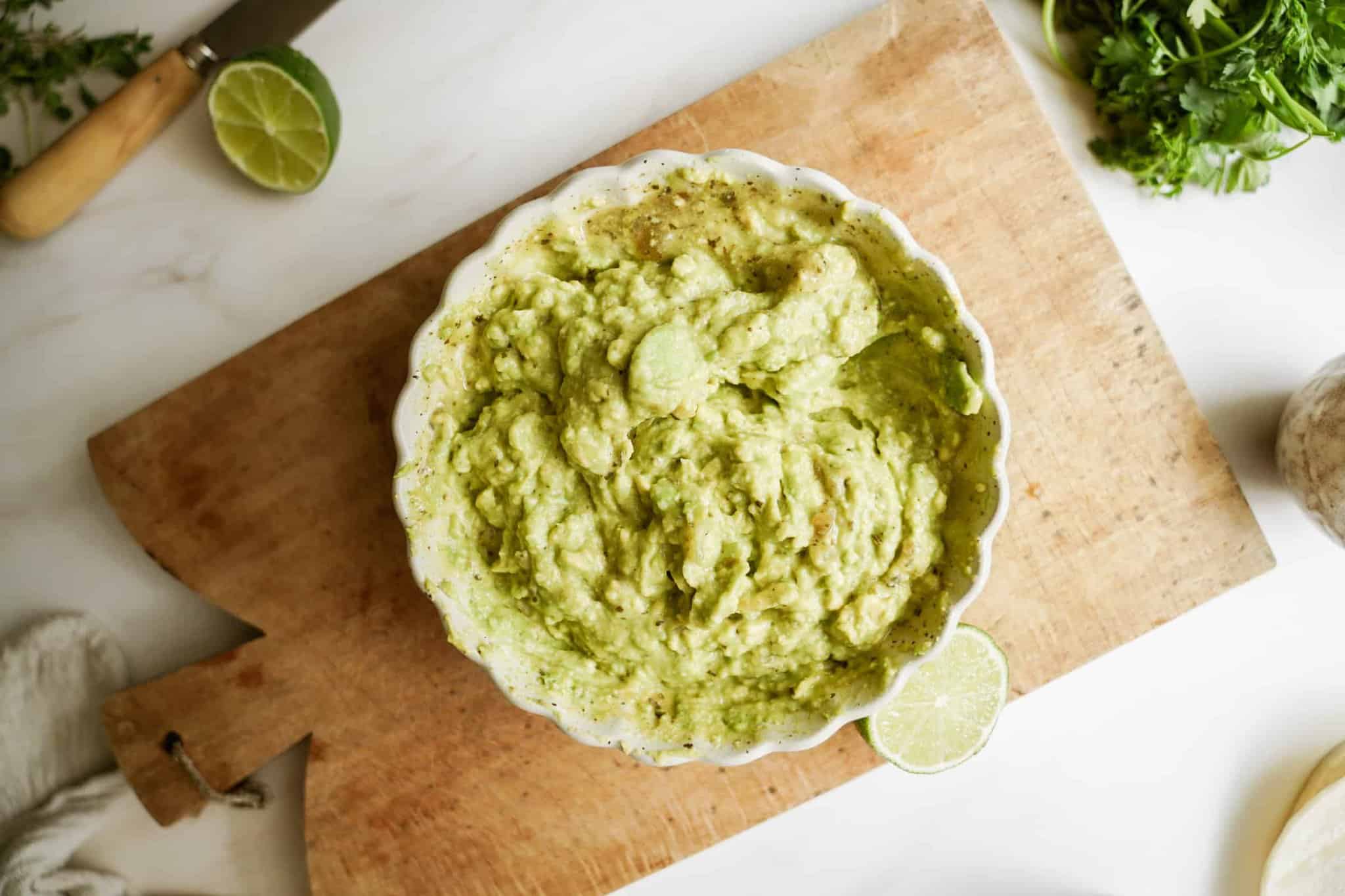 Mashed guacamole in a bowl on a cutting board