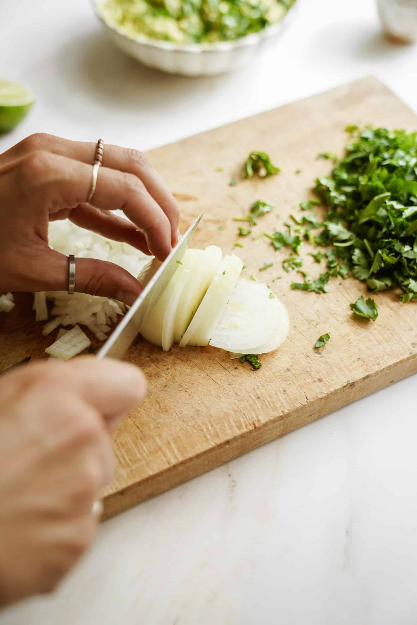 Hand chopping up white onion small on cutting board