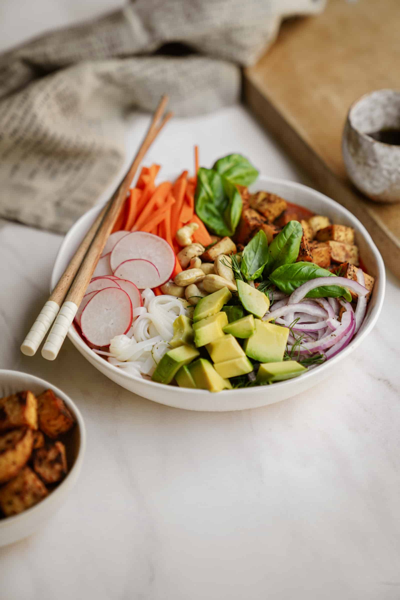 Crispy tofu noodle bowl on counter in white bowl with chopsticks