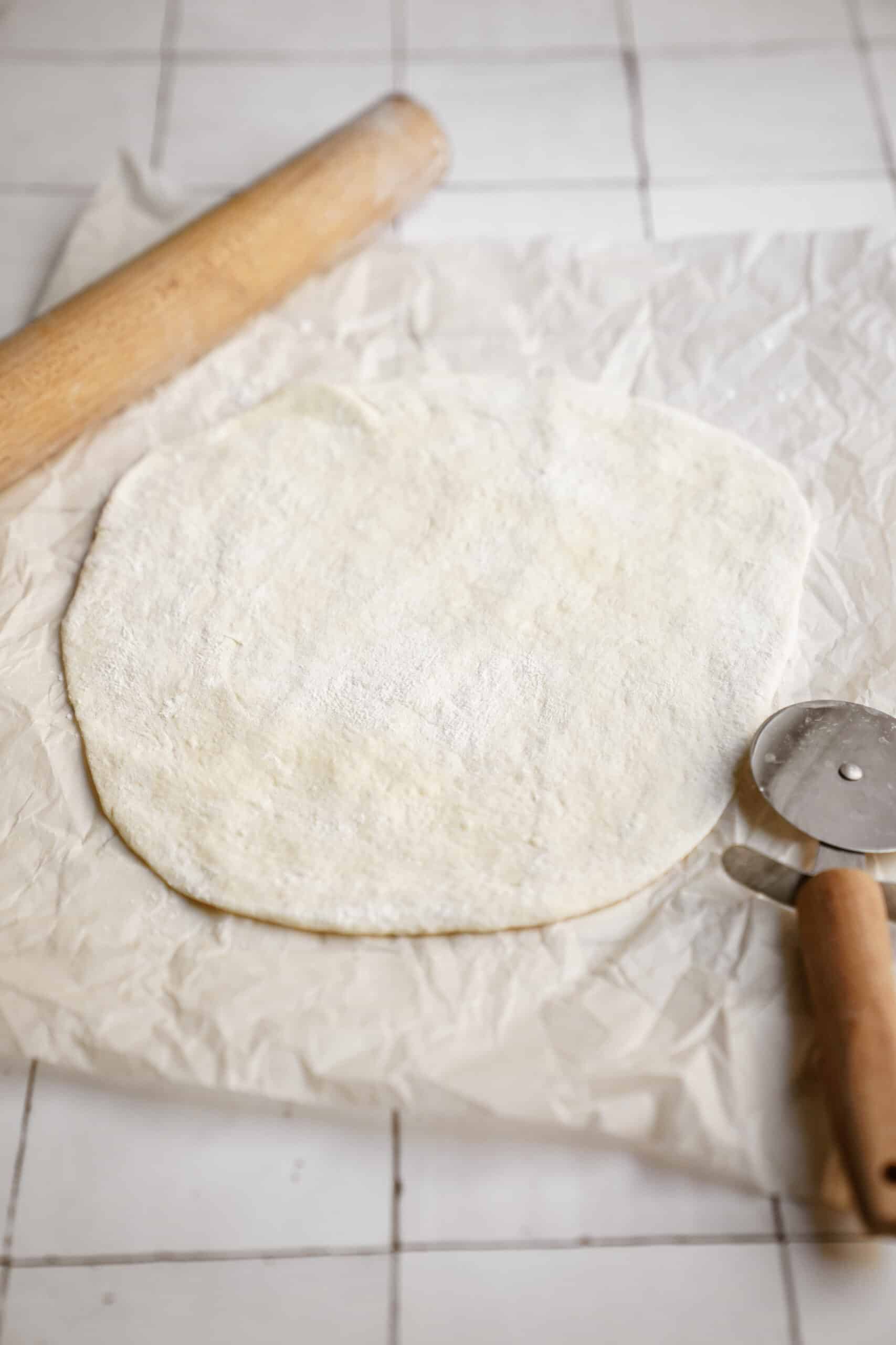 Pizza dough being rolled on parchment 