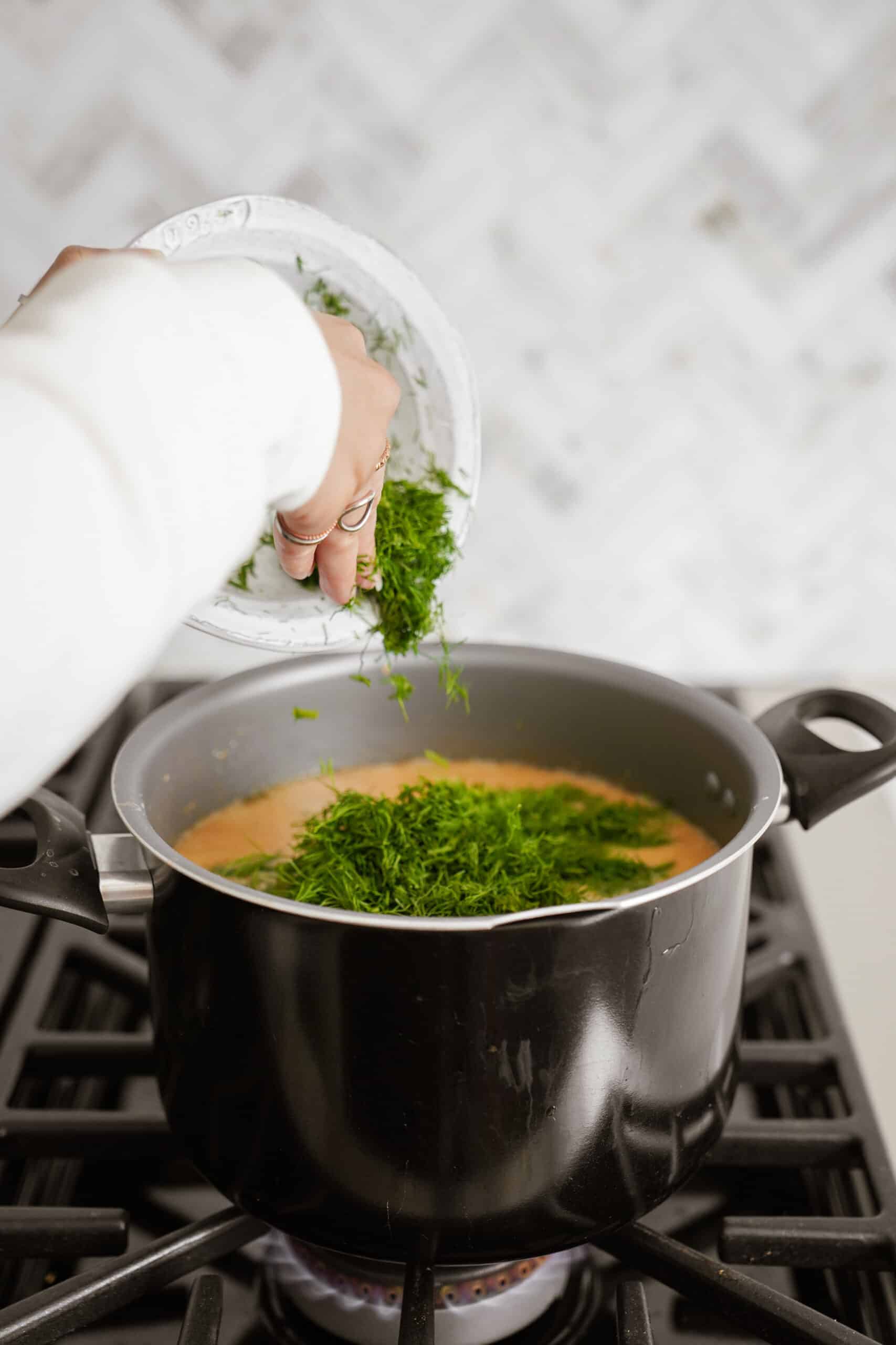 Fresh dill being added to pot on stove