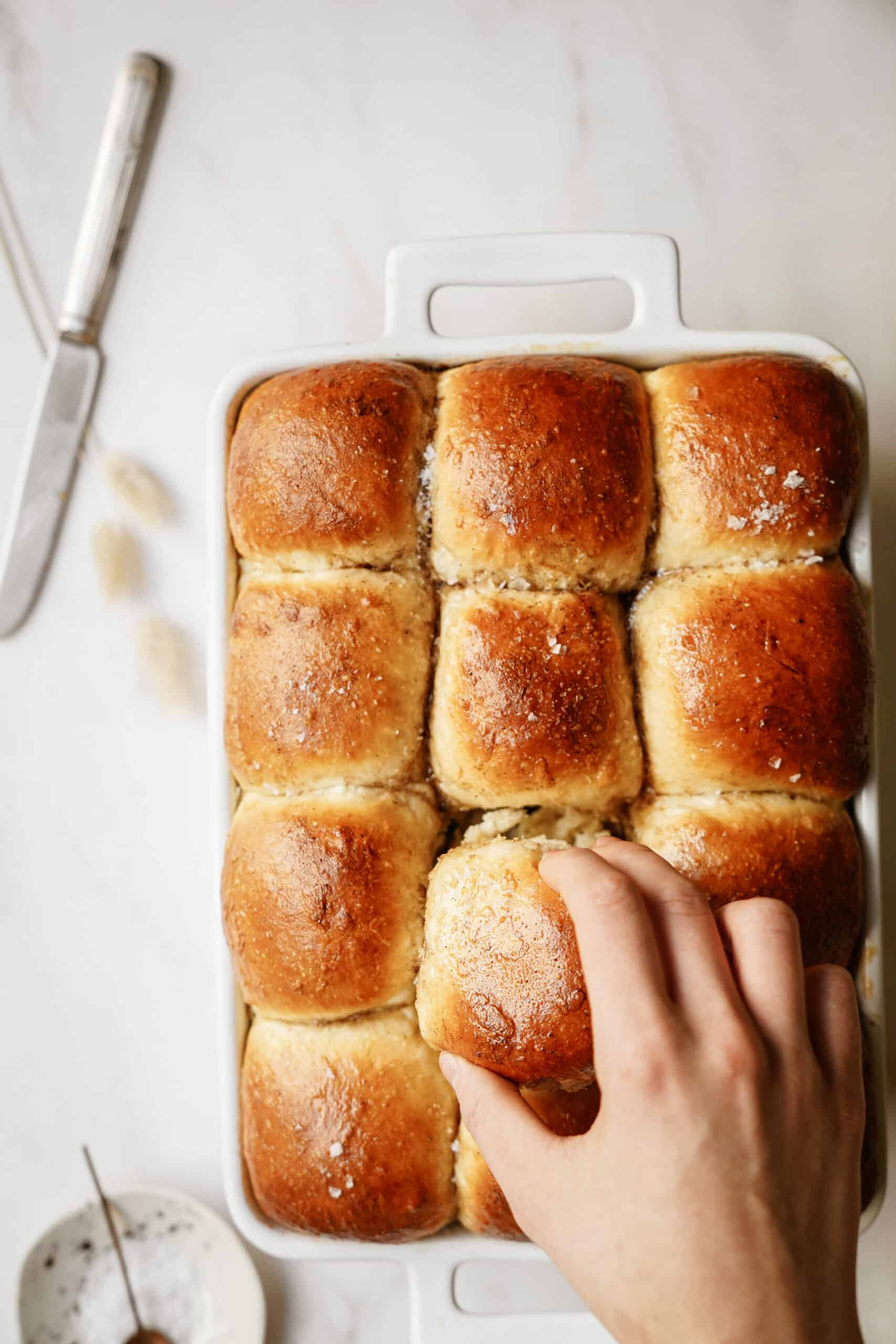 Hand taking dinner roll out of casserole dish