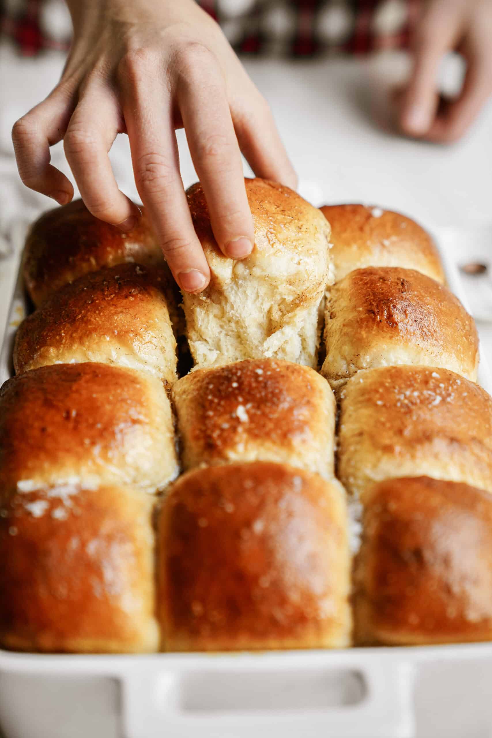 Hand taking dinner roll out of casserole dish