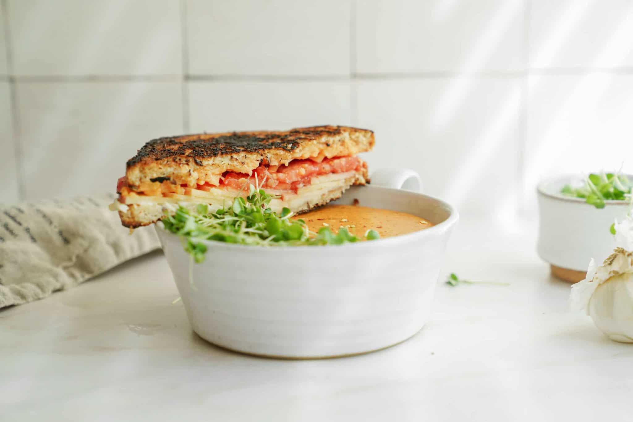 Creamy tomato soup in a white bowl with a sandwich on top