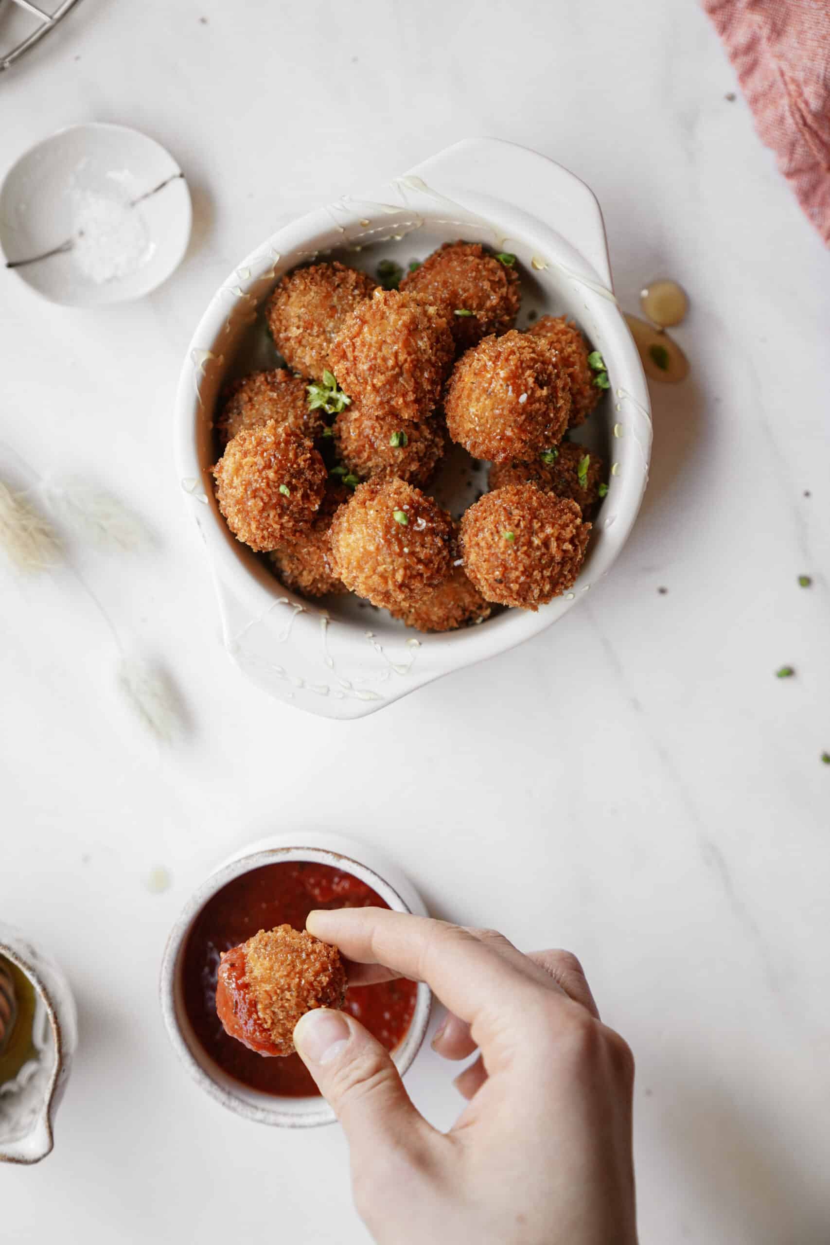 Hand dipping fried cheese ball in sauce