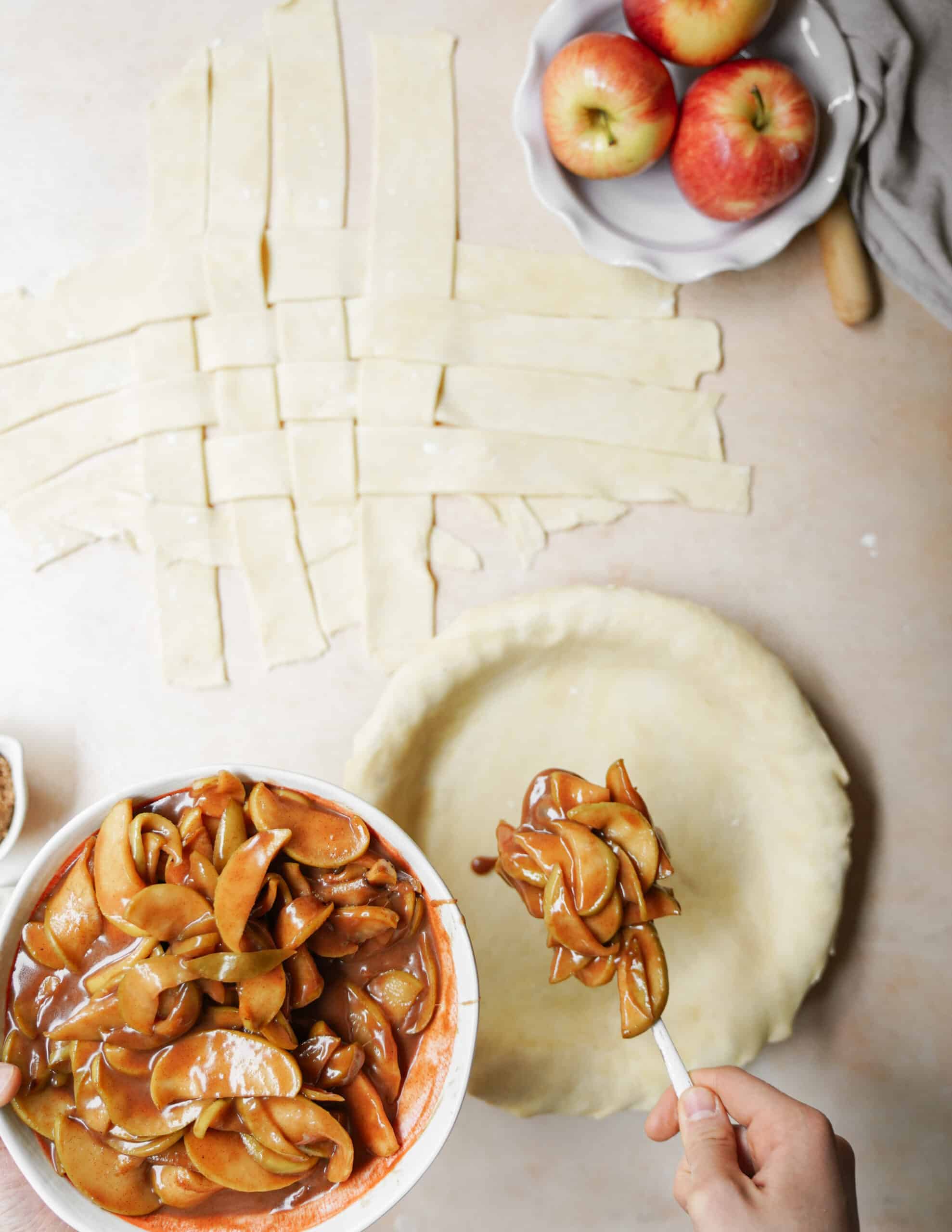 Apple pie filling being added to pie with latticework in the background