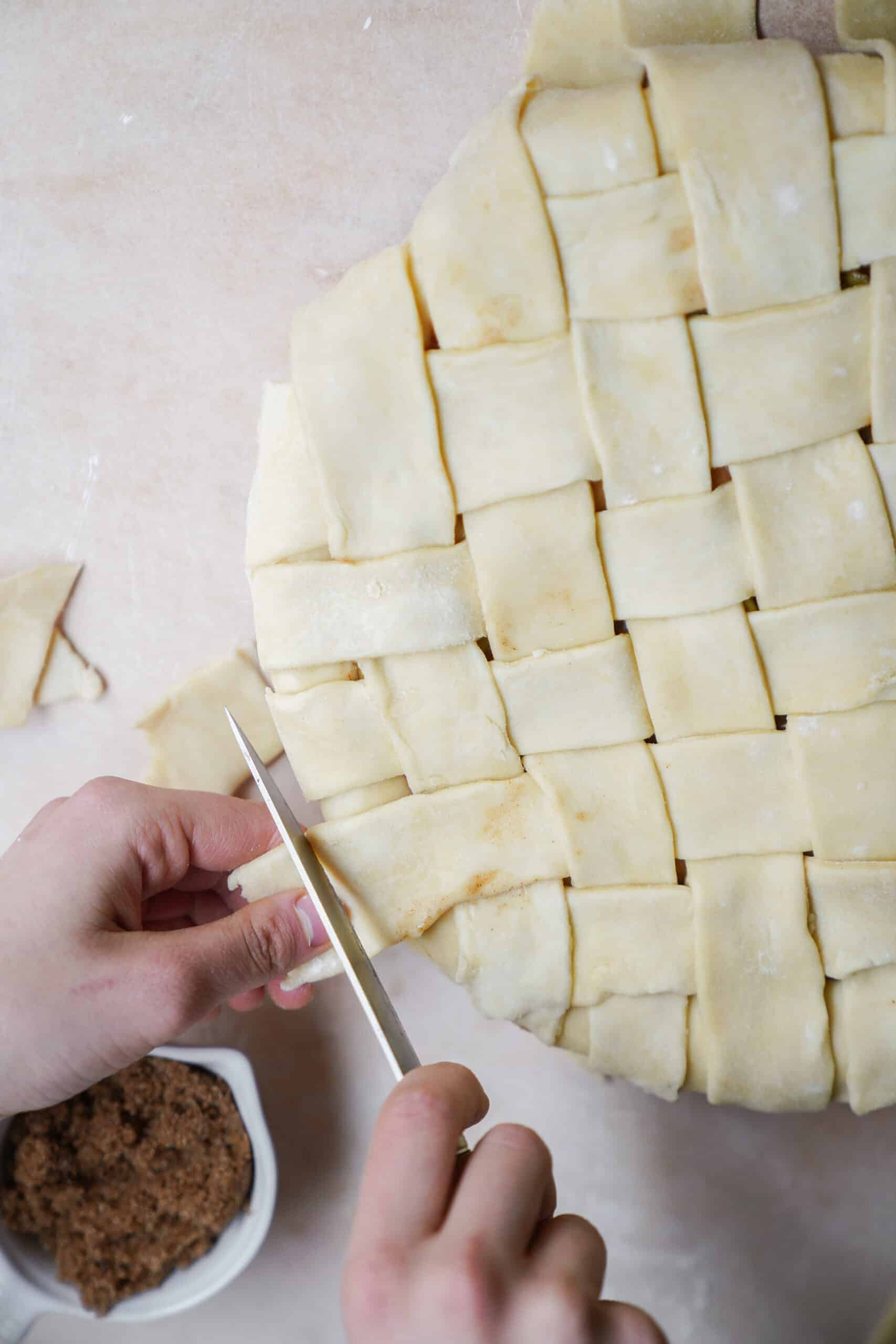 Hands trimming edges of apple pie