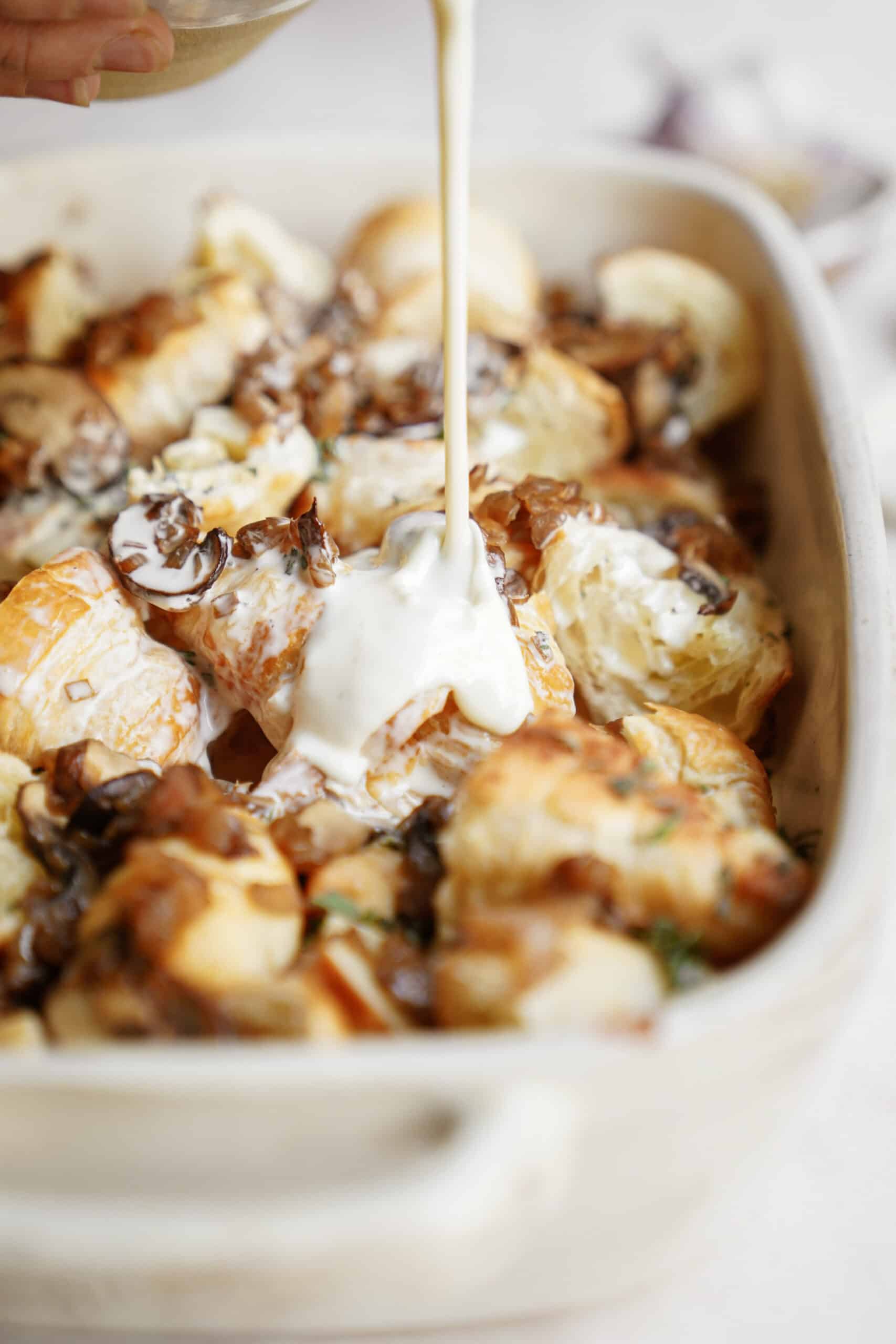 Creamy being poured on savory bread pudding