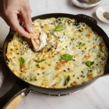 Spinach and Artichoke Dip in cast iron dish with hand dipping pita chip in