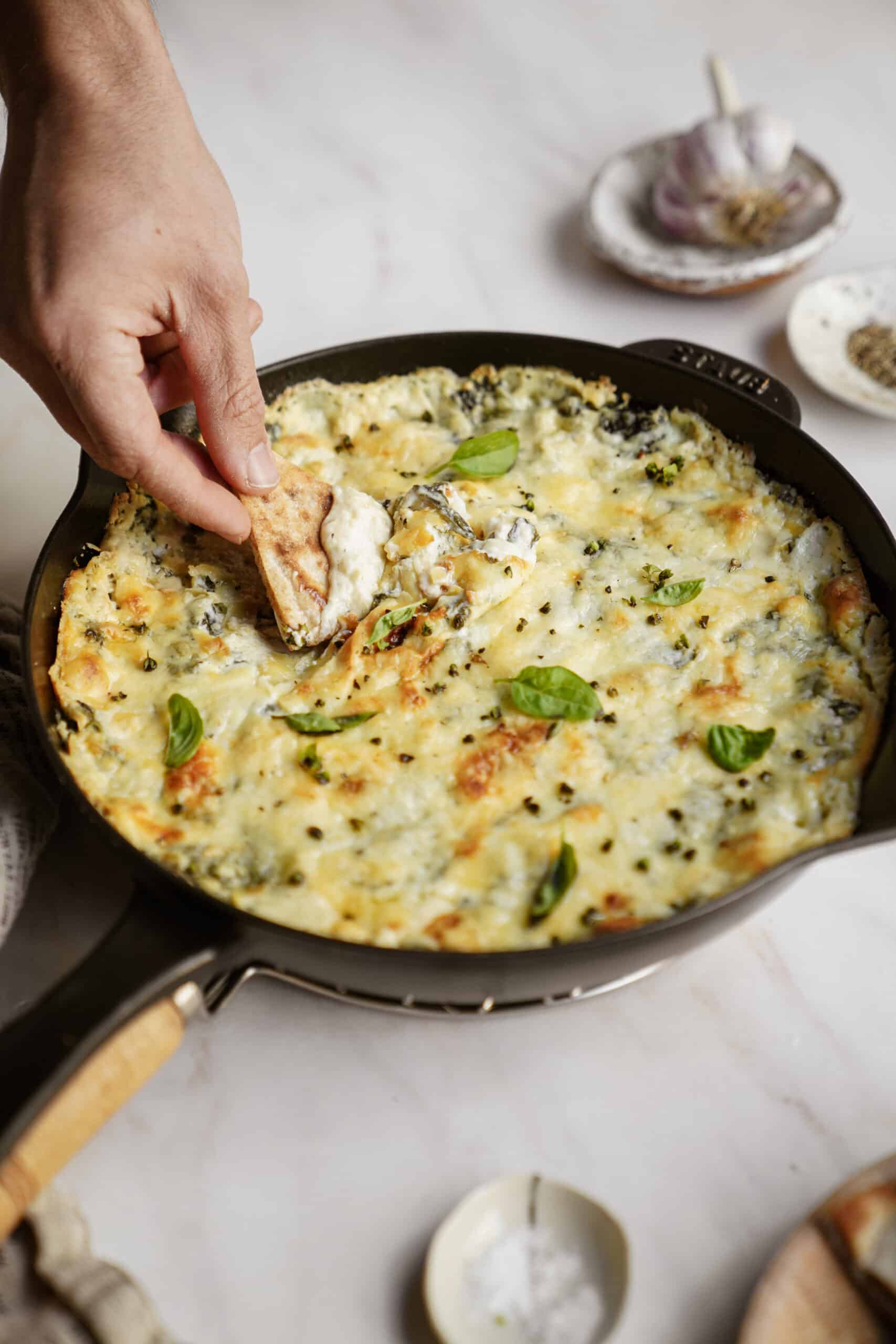 Spinach and Artichoke Dip in cast iron dish with hand dipping pita chip in