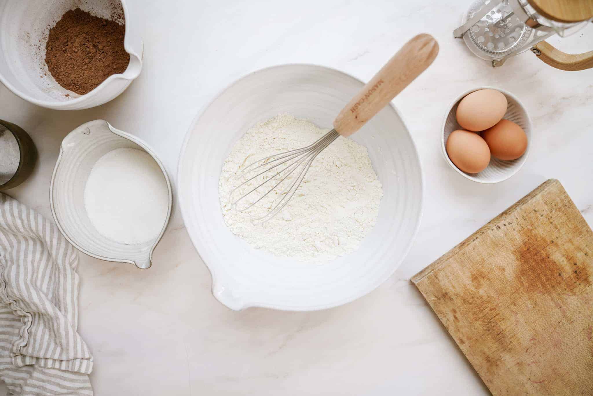 Flour in a bowl with a whisk and other ingredients around it
