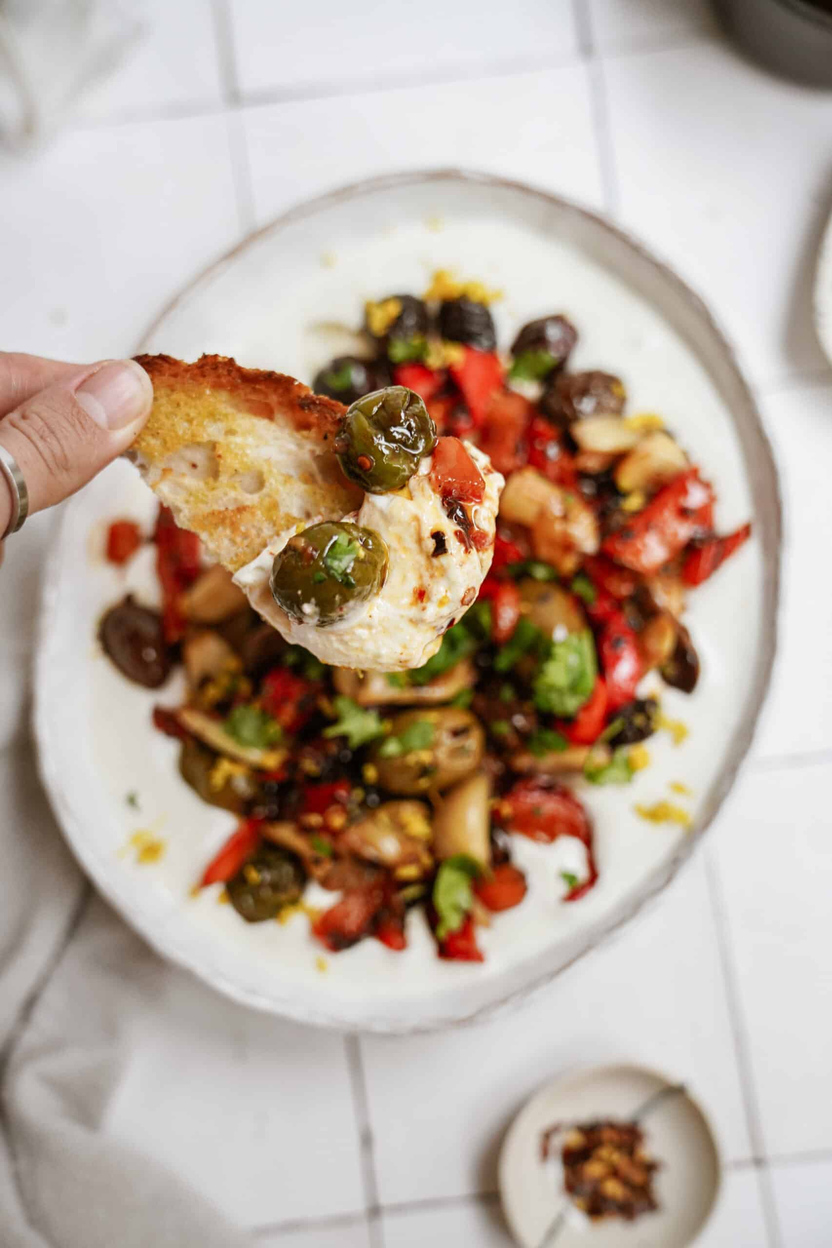 Whipped feta with roasted veggies in a serving bowl with bread dipping in 