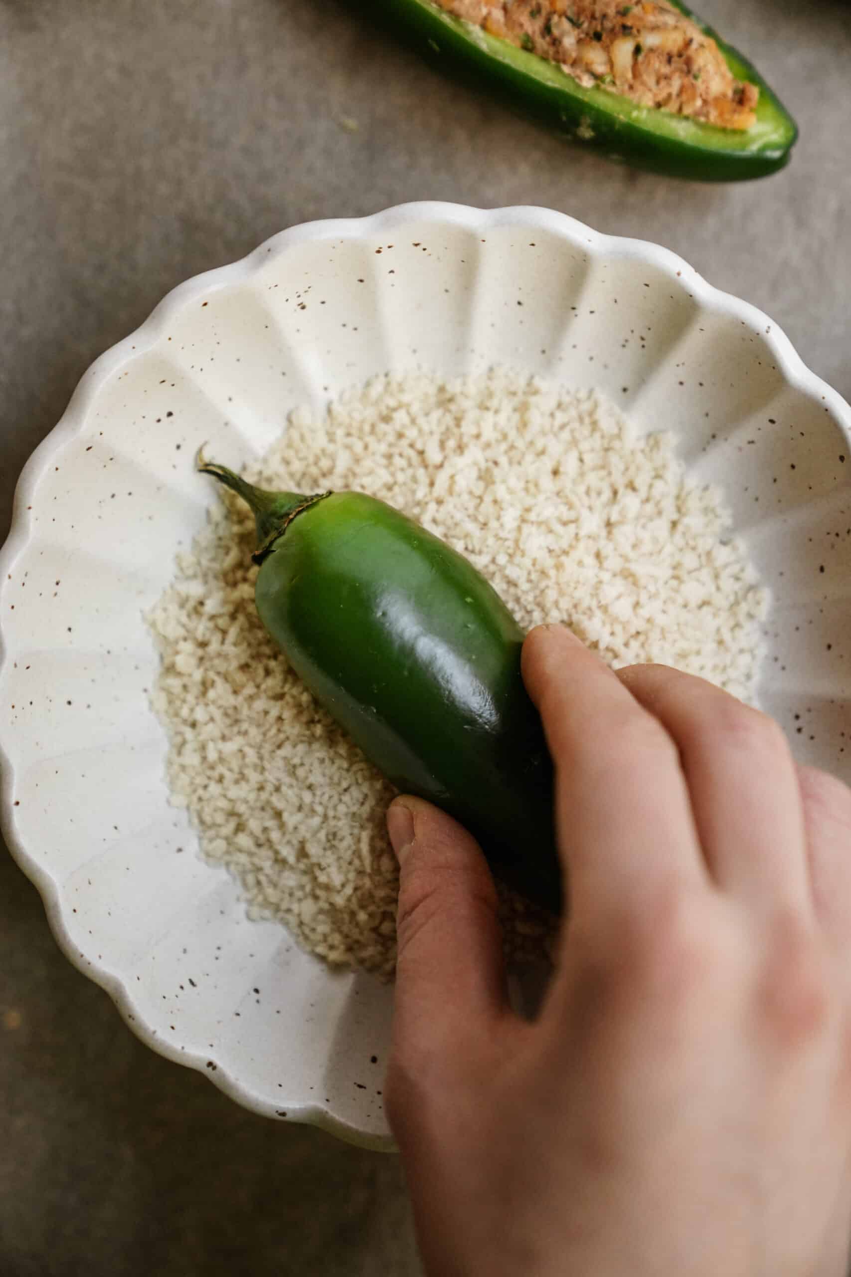 Dipping pepper into breadcrumbs, a step in how to make jalapeno poppers