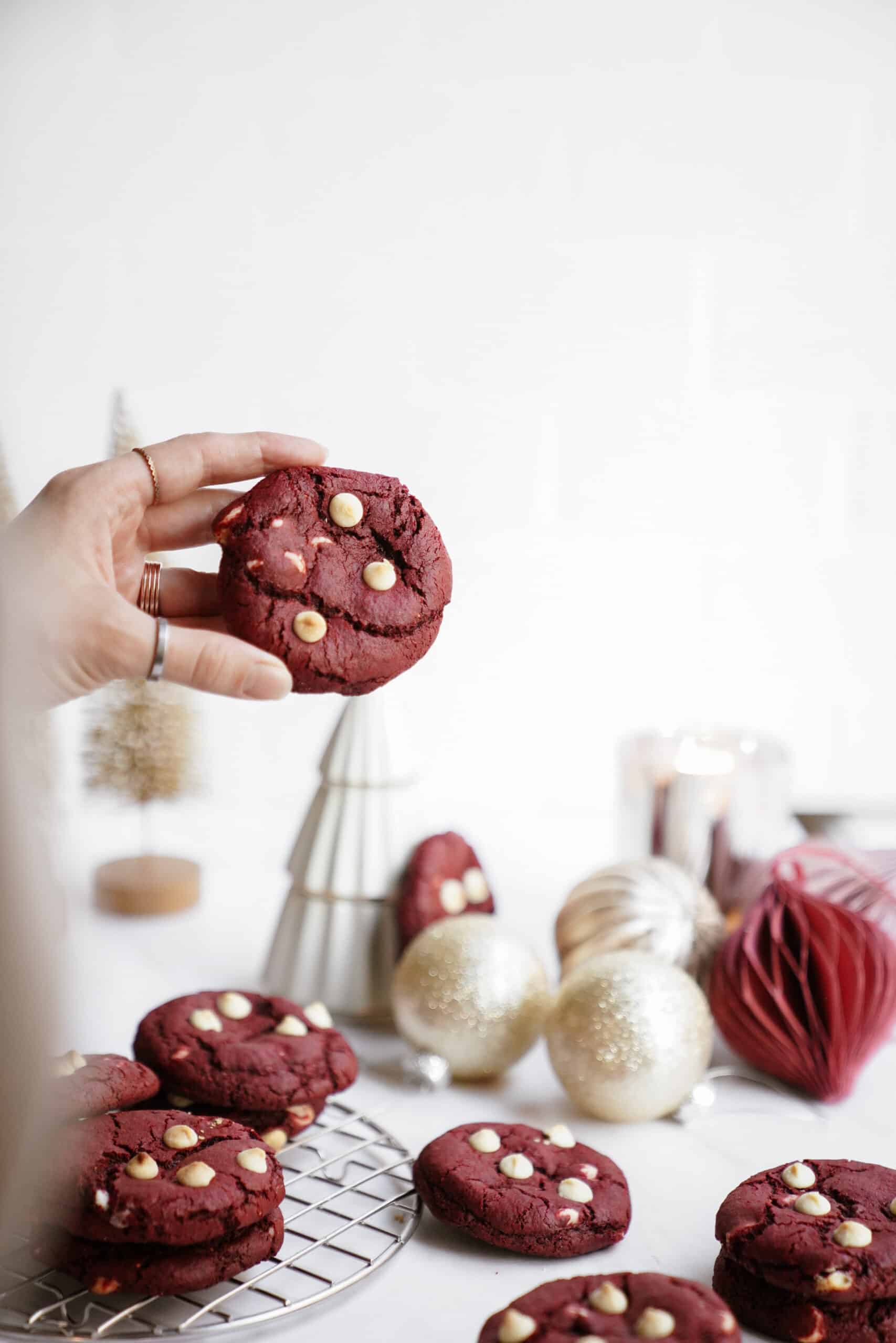 A hand picking up a red velvet cookie from a countertop