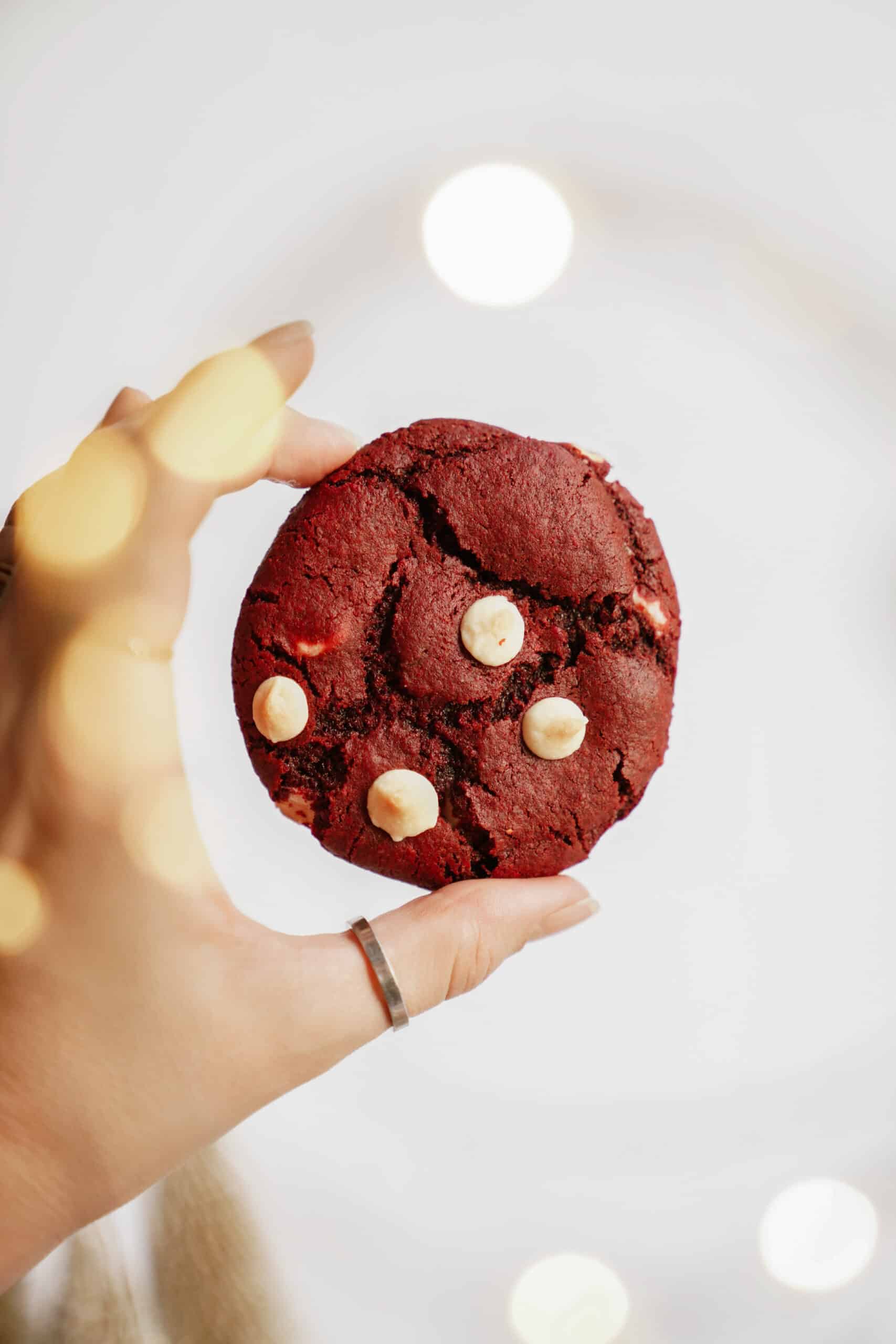 A hand holding a single red velvet cookie