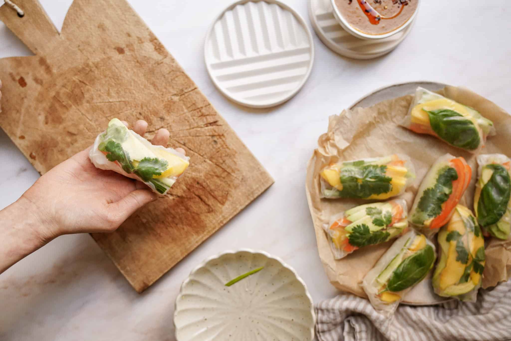 Hand holding a rice paper roll over a cutting board