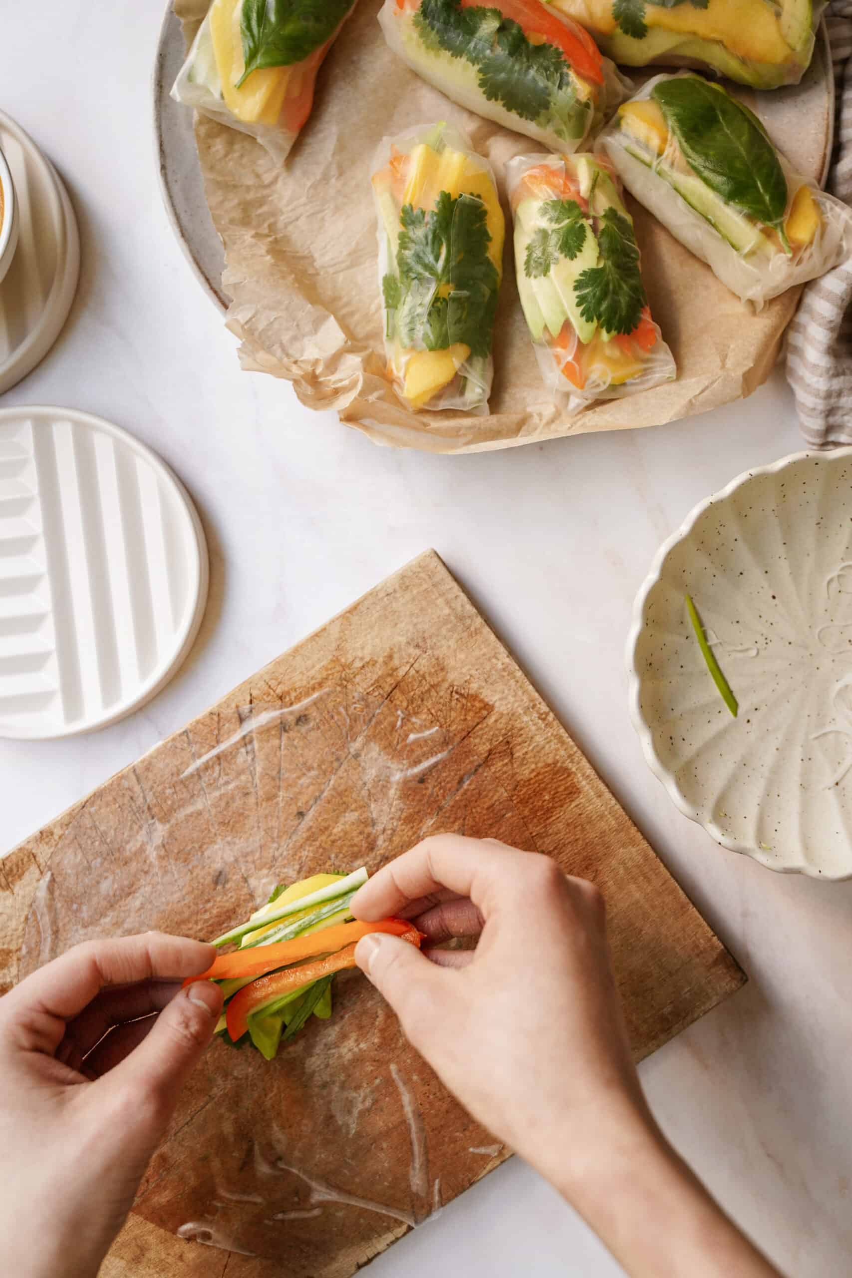 Hands putting fresh ingredients on rice paper for salad rolls