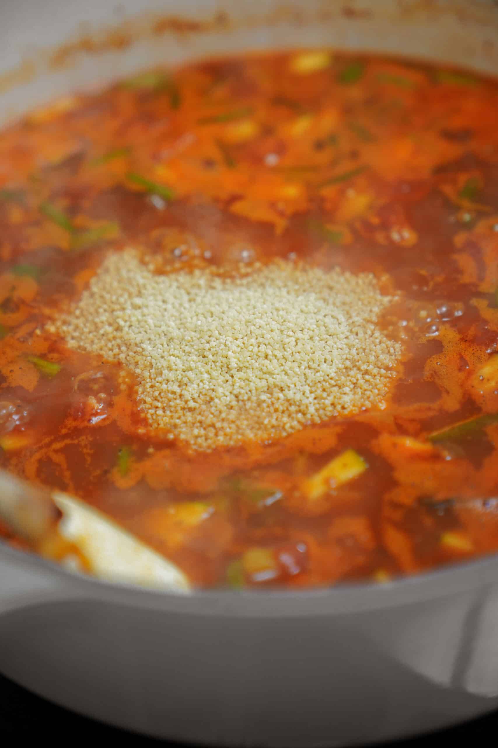 Pasta being added to minestrone soup recipe in a pot