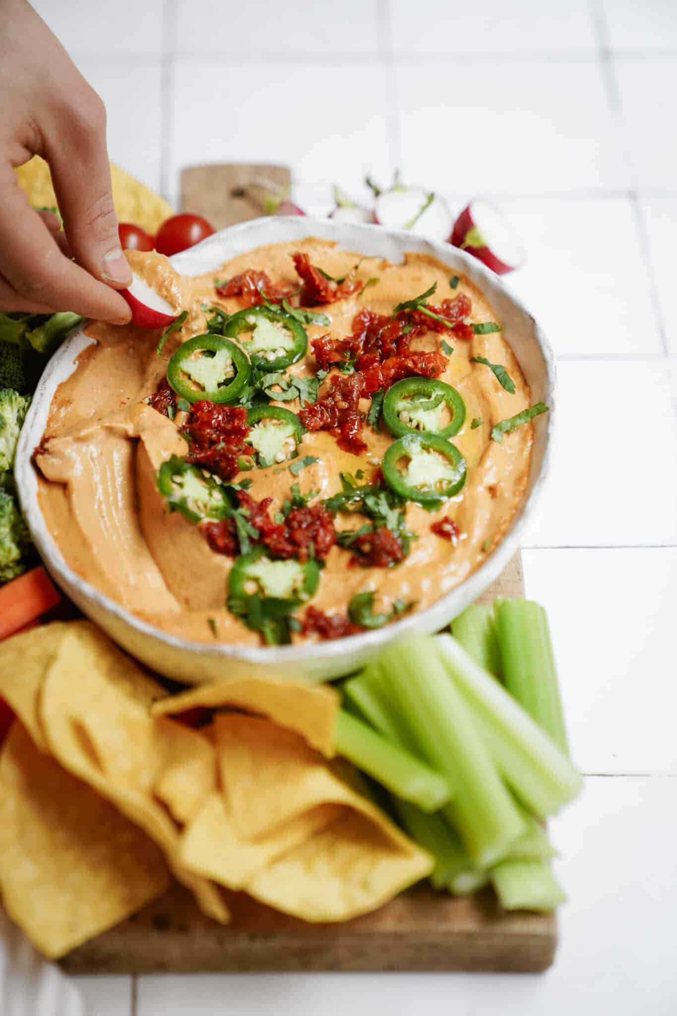 Hand dipping fresh veggies into homemade queso sauce recipe