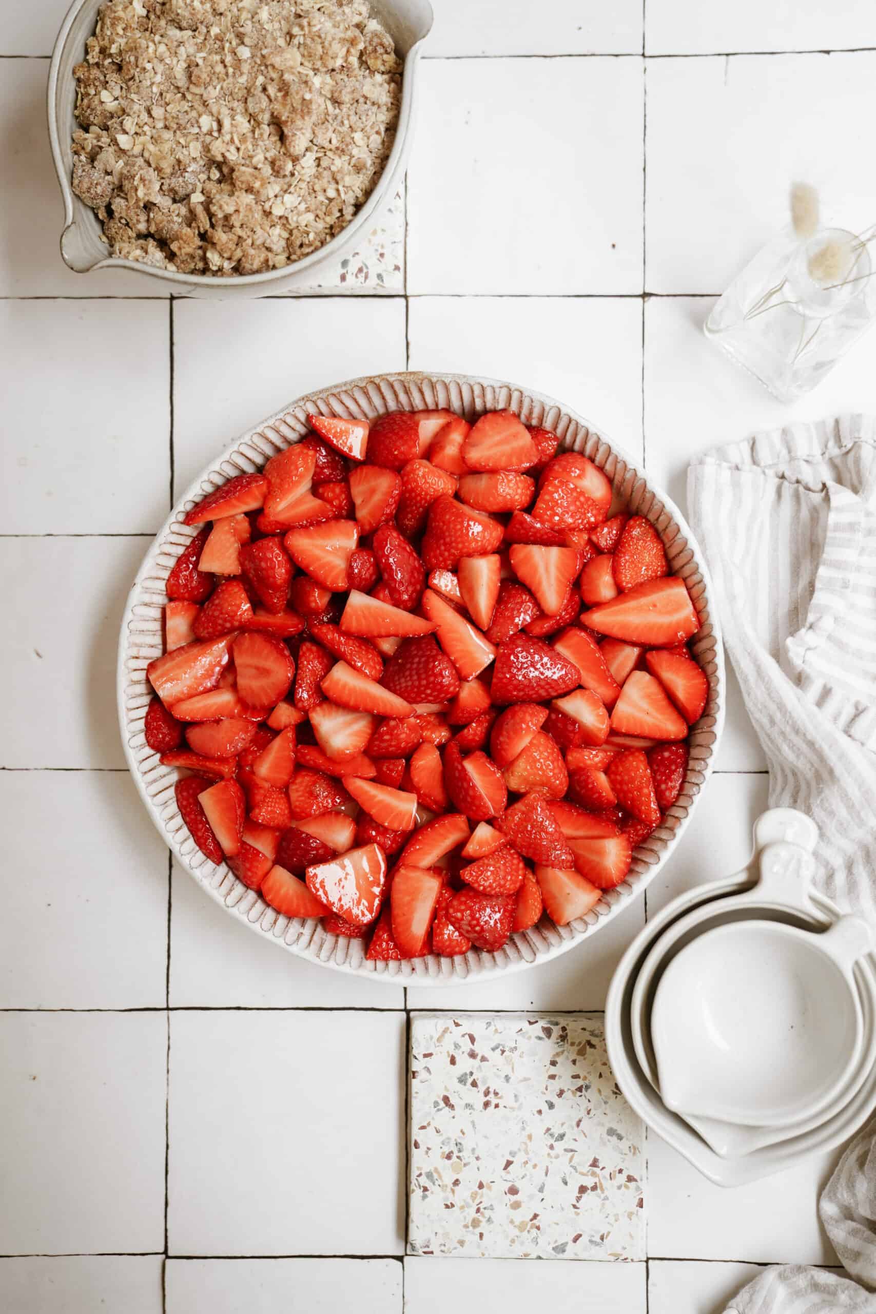 Bowl of fresh strawberries with ingredients around them for strawberry crumble