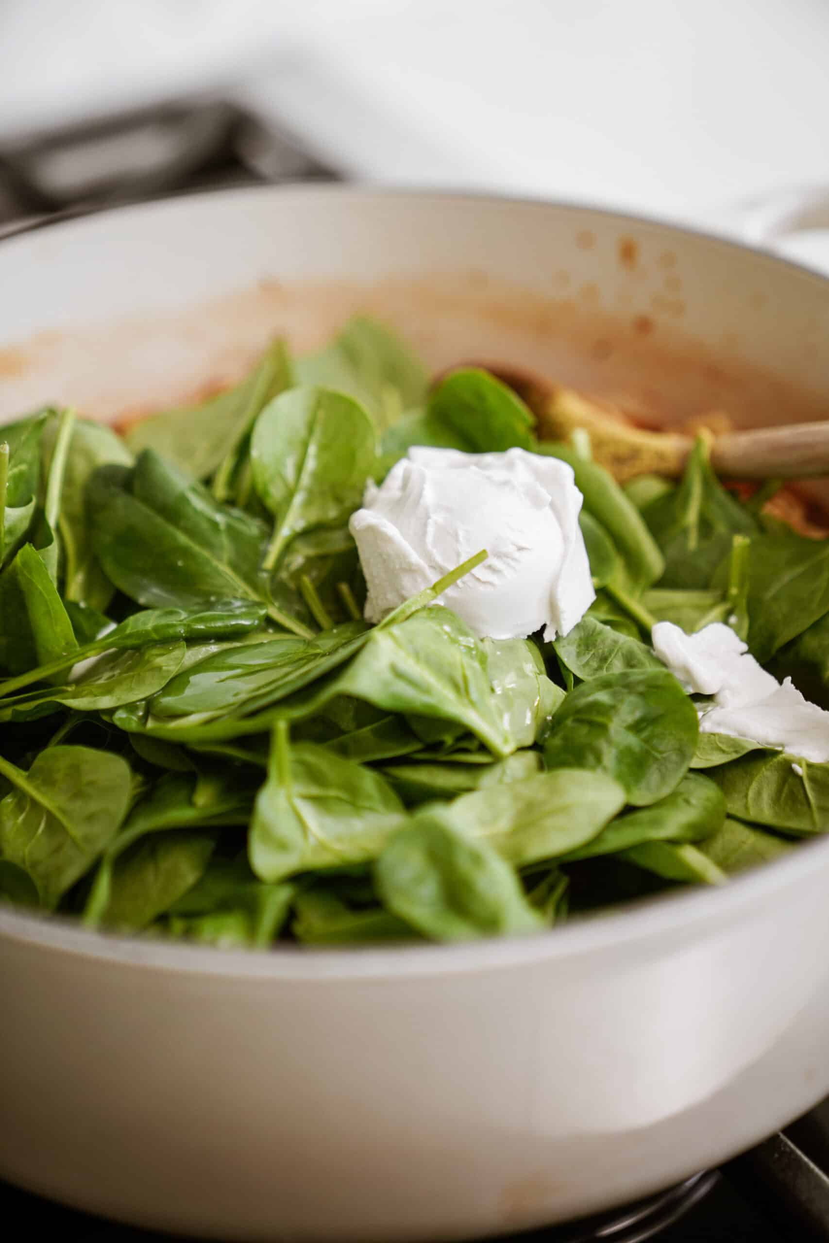 Spinach and cream being added to the soup pot on stove