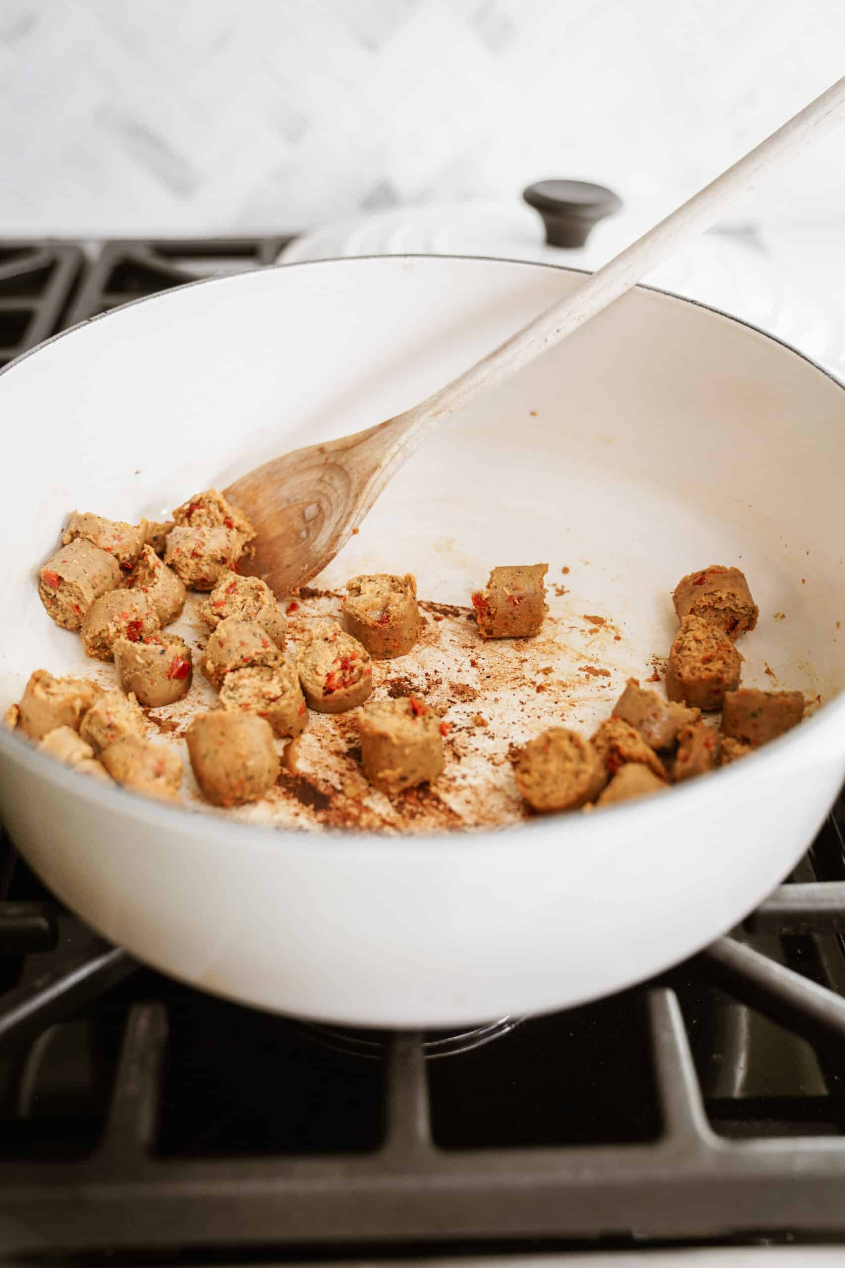 Sausages cooking in pot with a wooden spoon