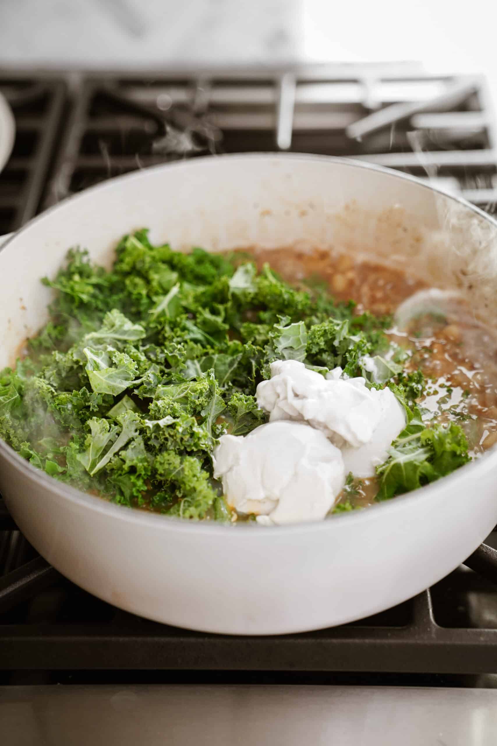 Adding in kale to zuppa toscana in a pot