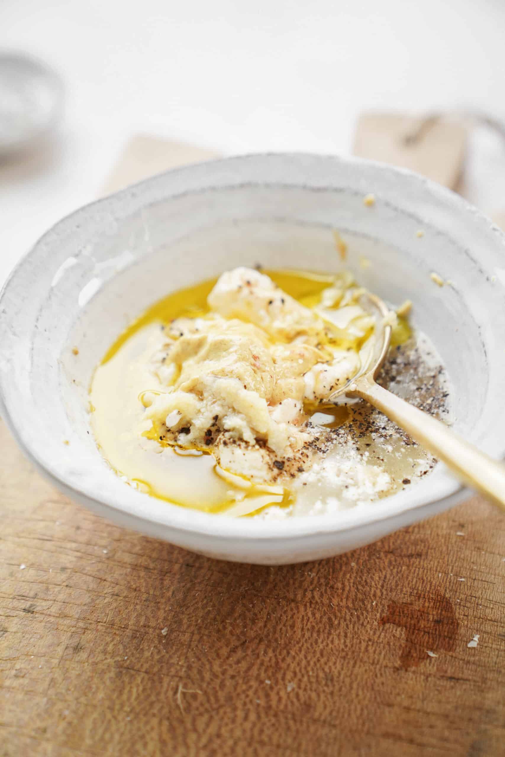 Ingredients for caesar salad dressing recipe in a bowl with a spoon