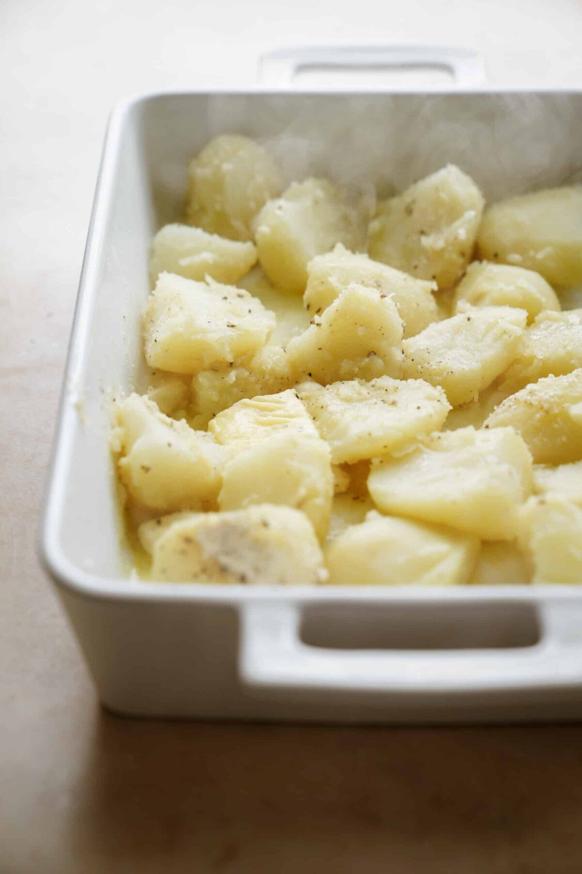 Cooked potatoes in a casserole dish covered with salt & pepper, onion powder, oil, garlic, and/or butter. Next step is to put them in the oven. 