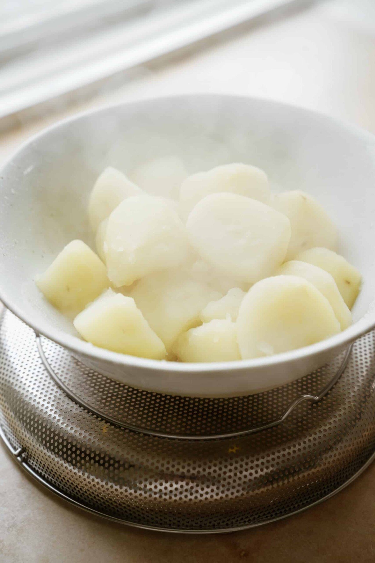 Cut and peeled potatoes in a white bowl on counter after boiling. 