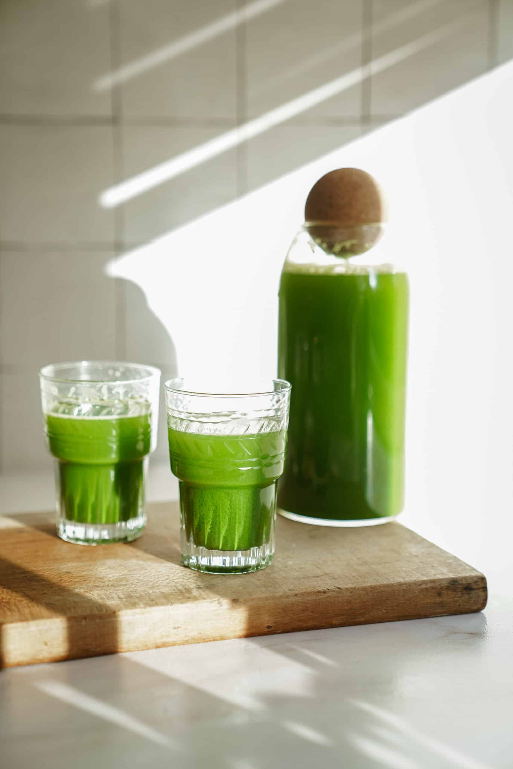 Green juice recipe in 2 glasses on a counter with a jug of juice