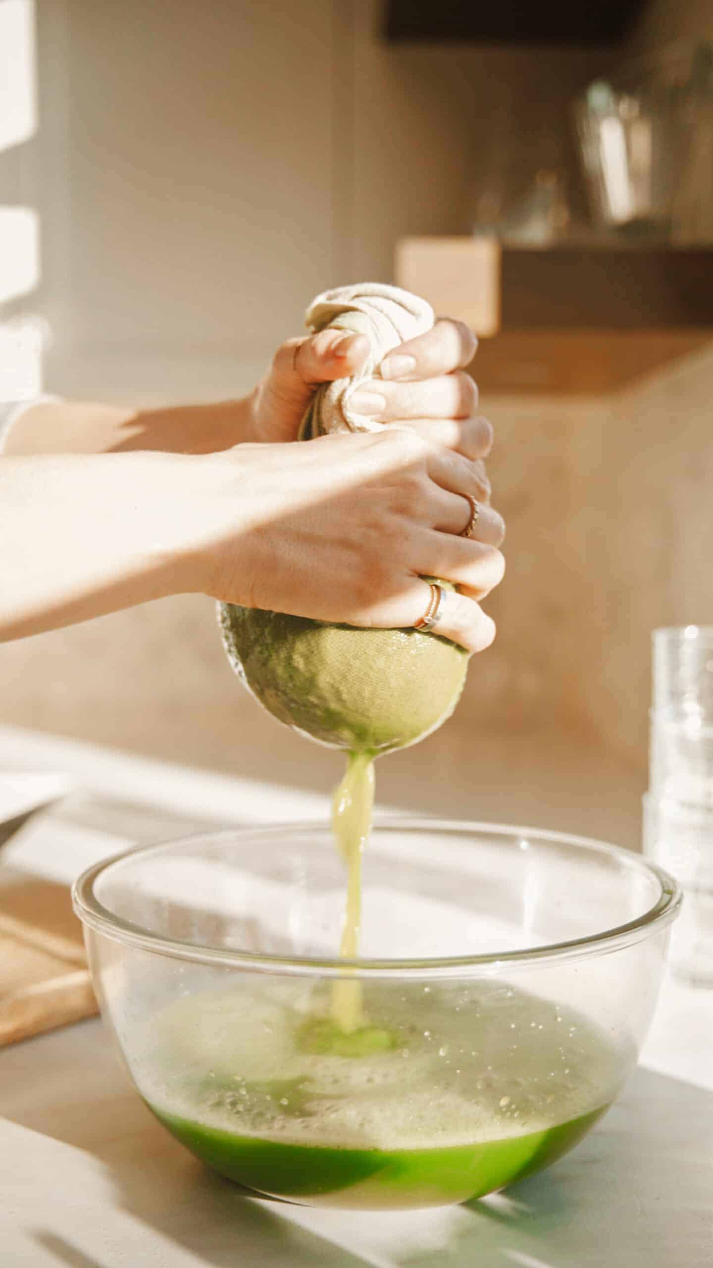 Using a cheesecloth to strain green juice into bowl