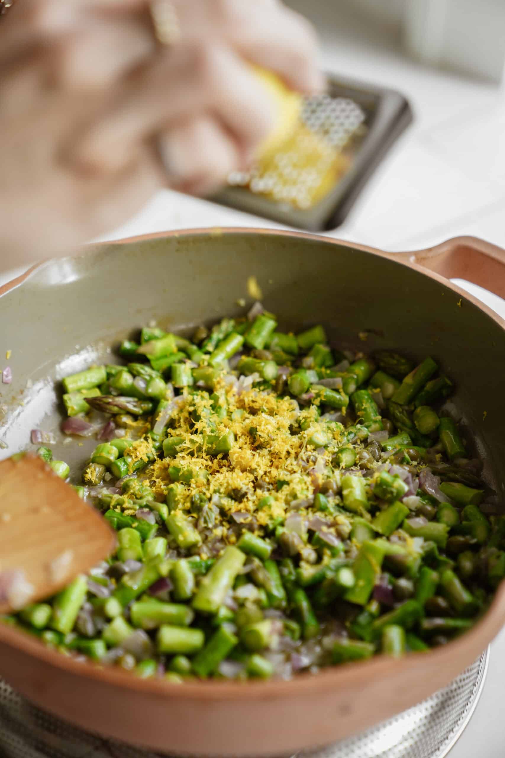 Asparagus being cooked in a pan with lemon zest being added