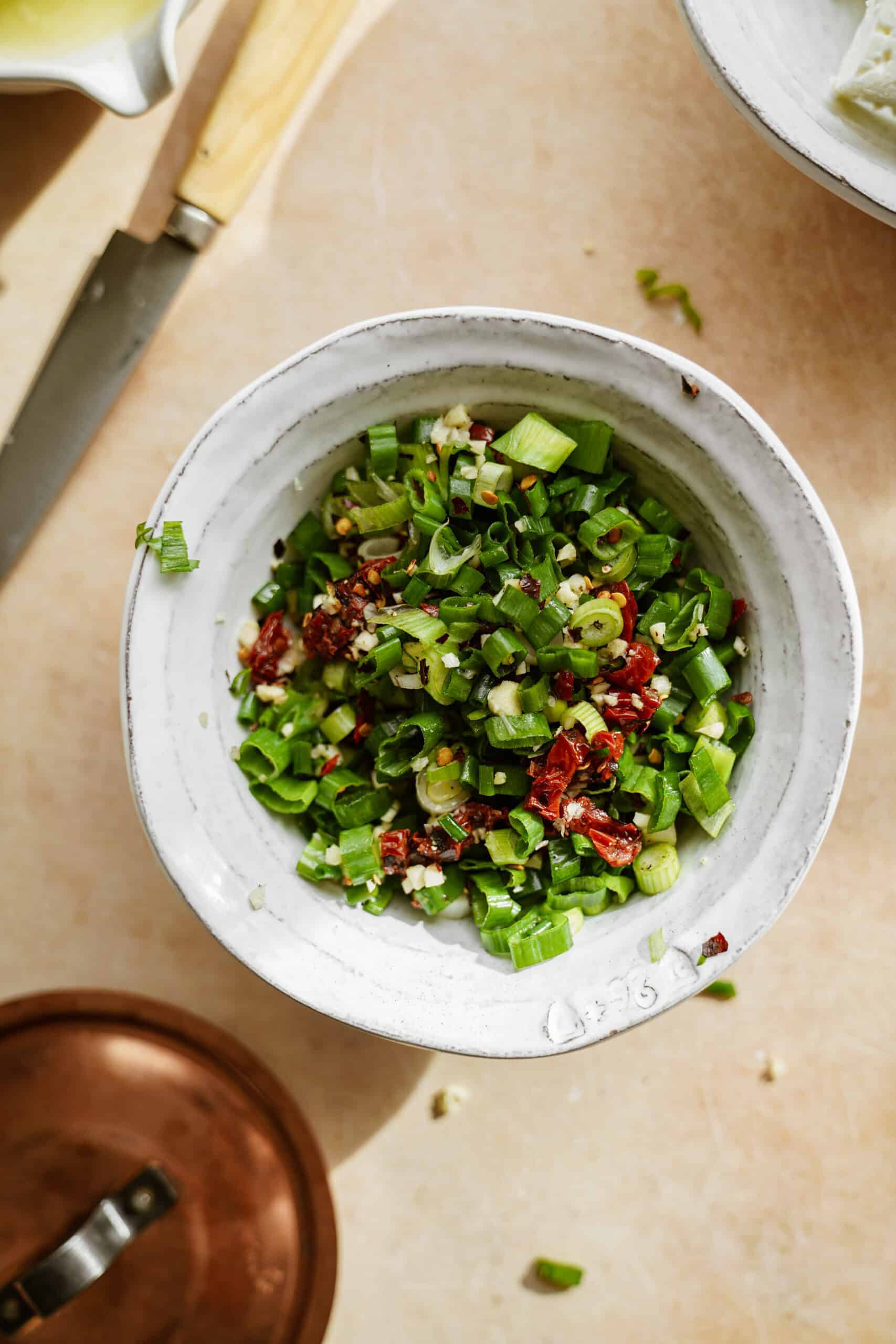 green onions and sun dried tomatoes chopping in a bowl