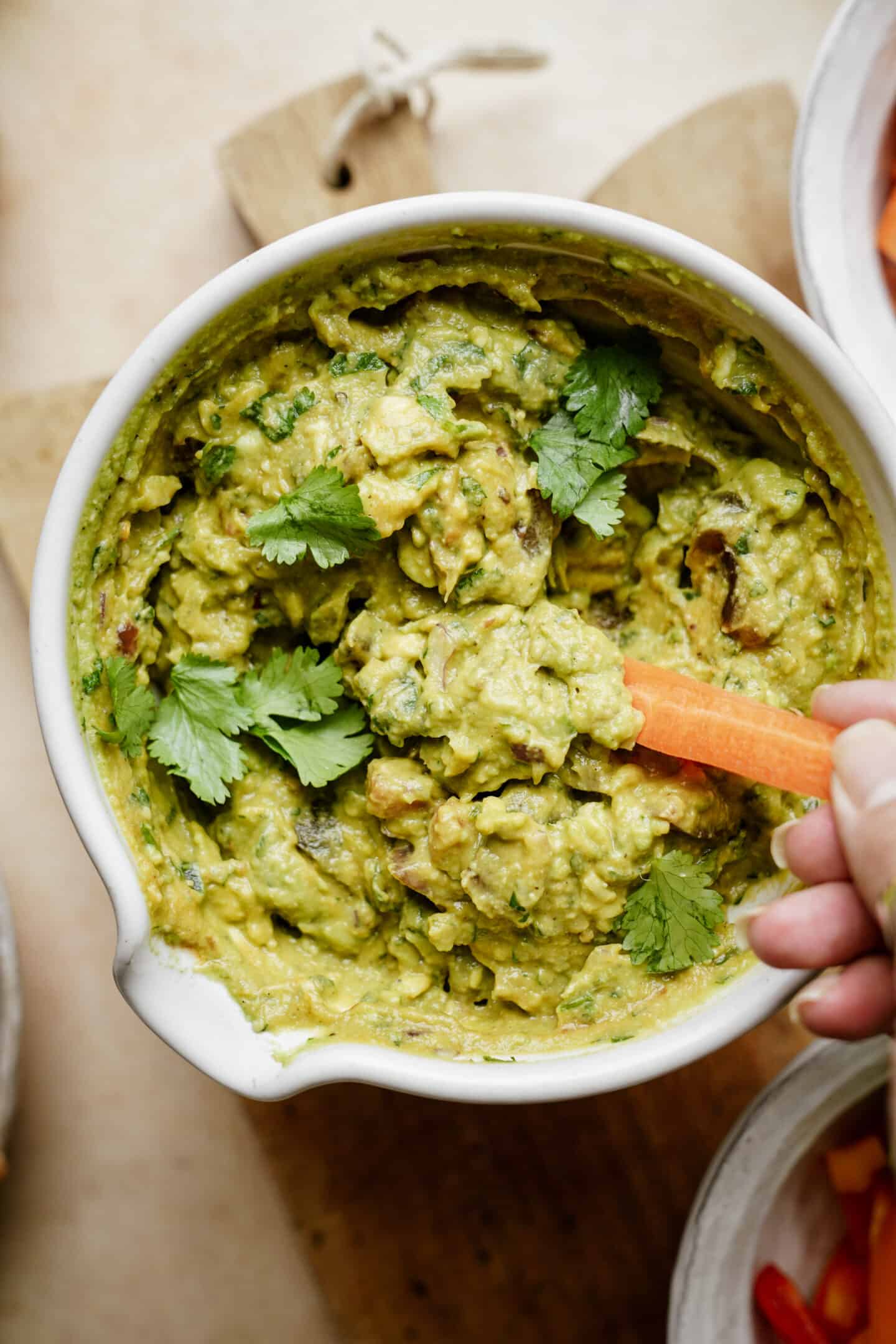 A big bowl of guacamole with a carrot dipping into it